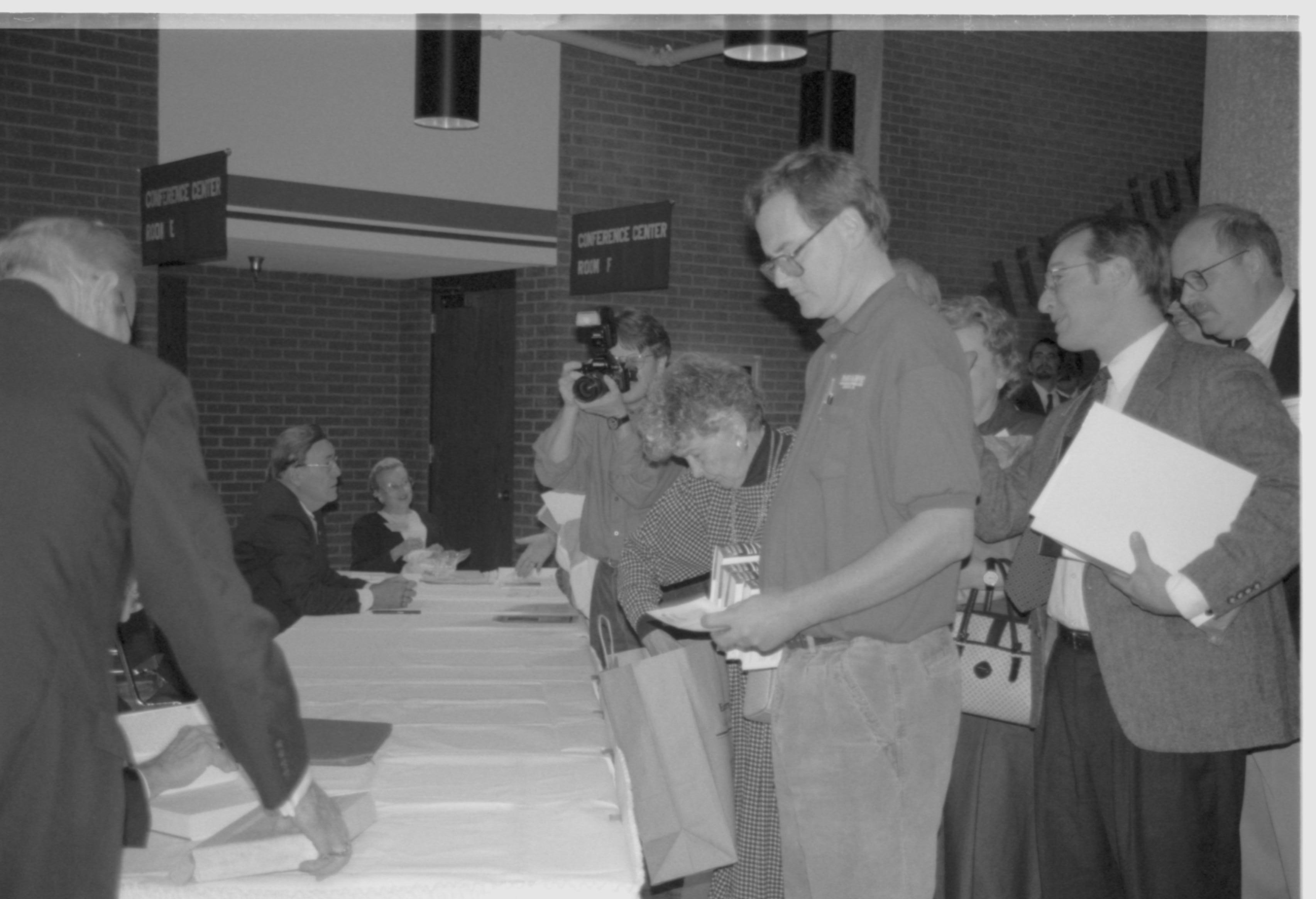 Attendees standing at empty table. Lincoln Colloquium; 88257 Lincoln, Colloquium