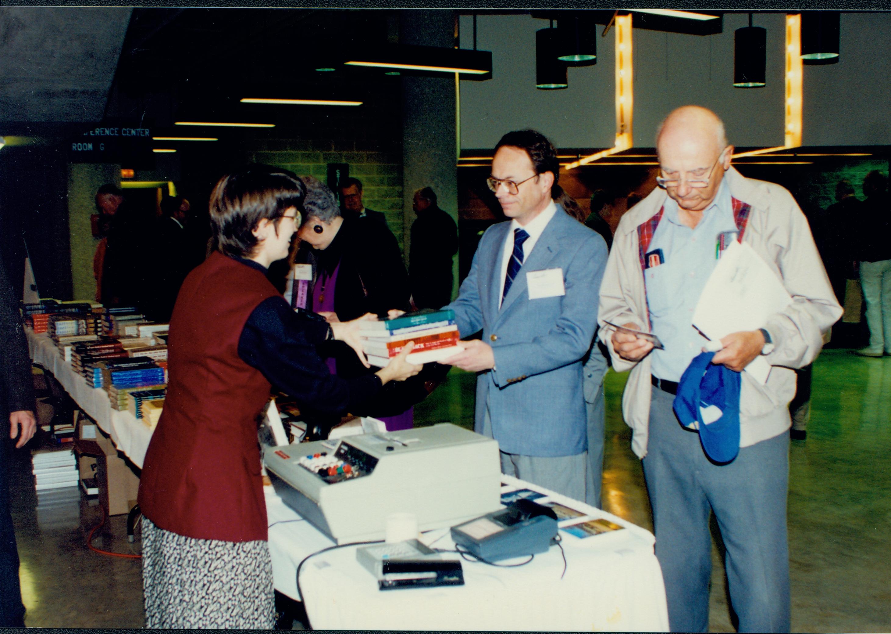 Man handing book purchase to lady. Lincoln Colloquium; 56935 Lincoln, Colloquium