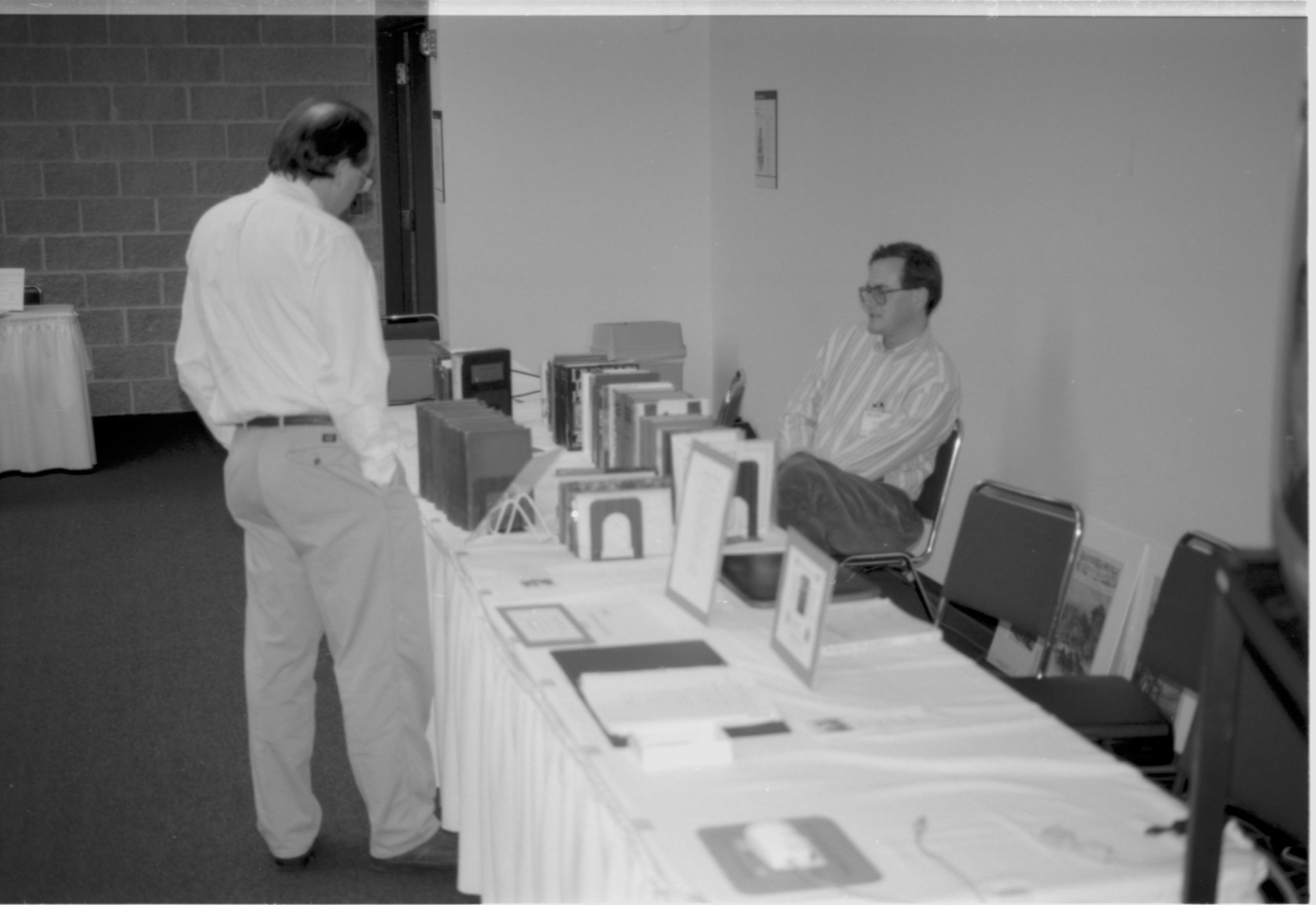 Man standing at book table, one seated. Lincoln Colloquium; UIS Roll#1, 4of4 Lincoln, Colloquium