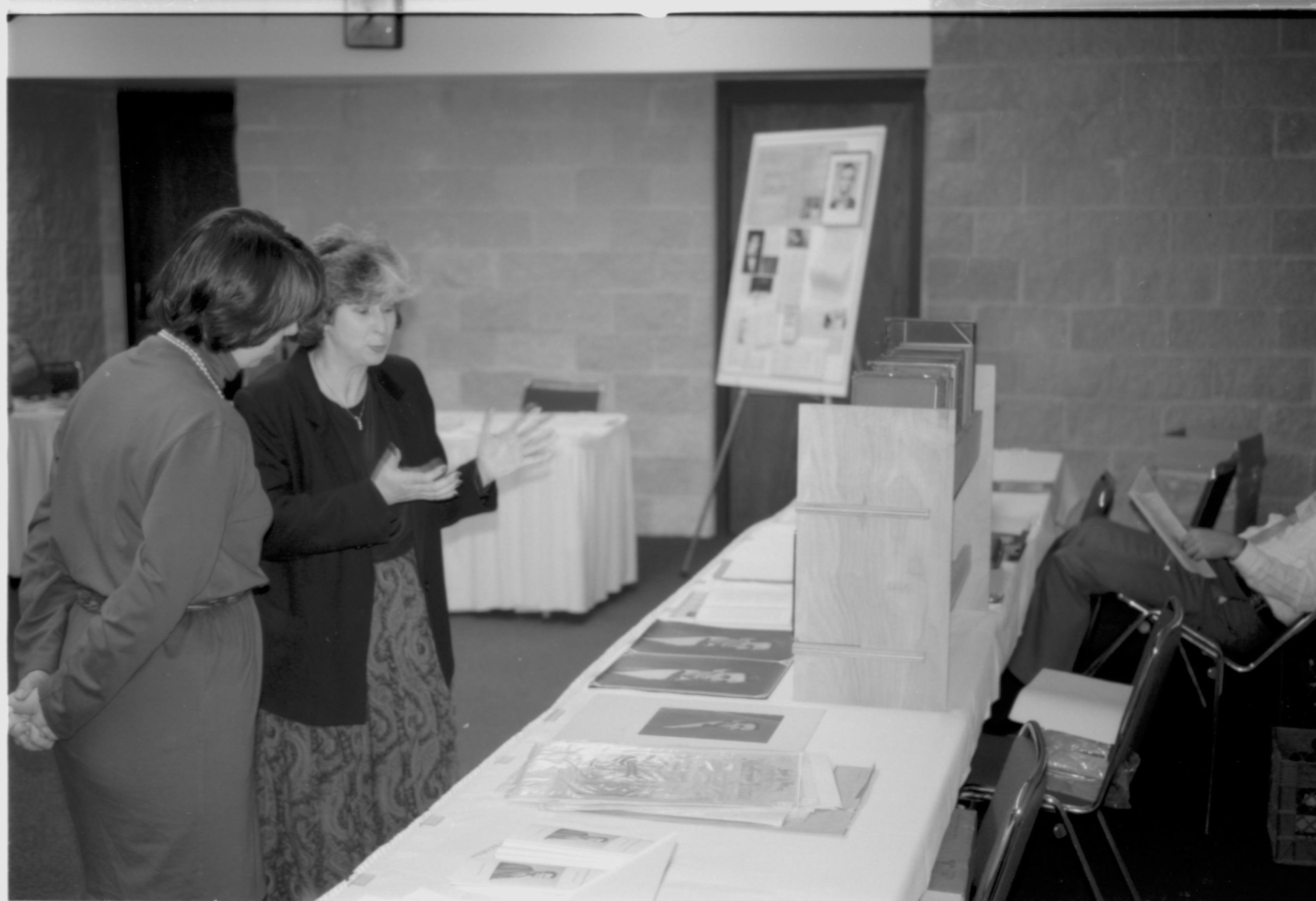 Two ladies talking at display table. Lincoln Colloquium; UIS Roll#1, 4of4 Lincoln, Colloquium
