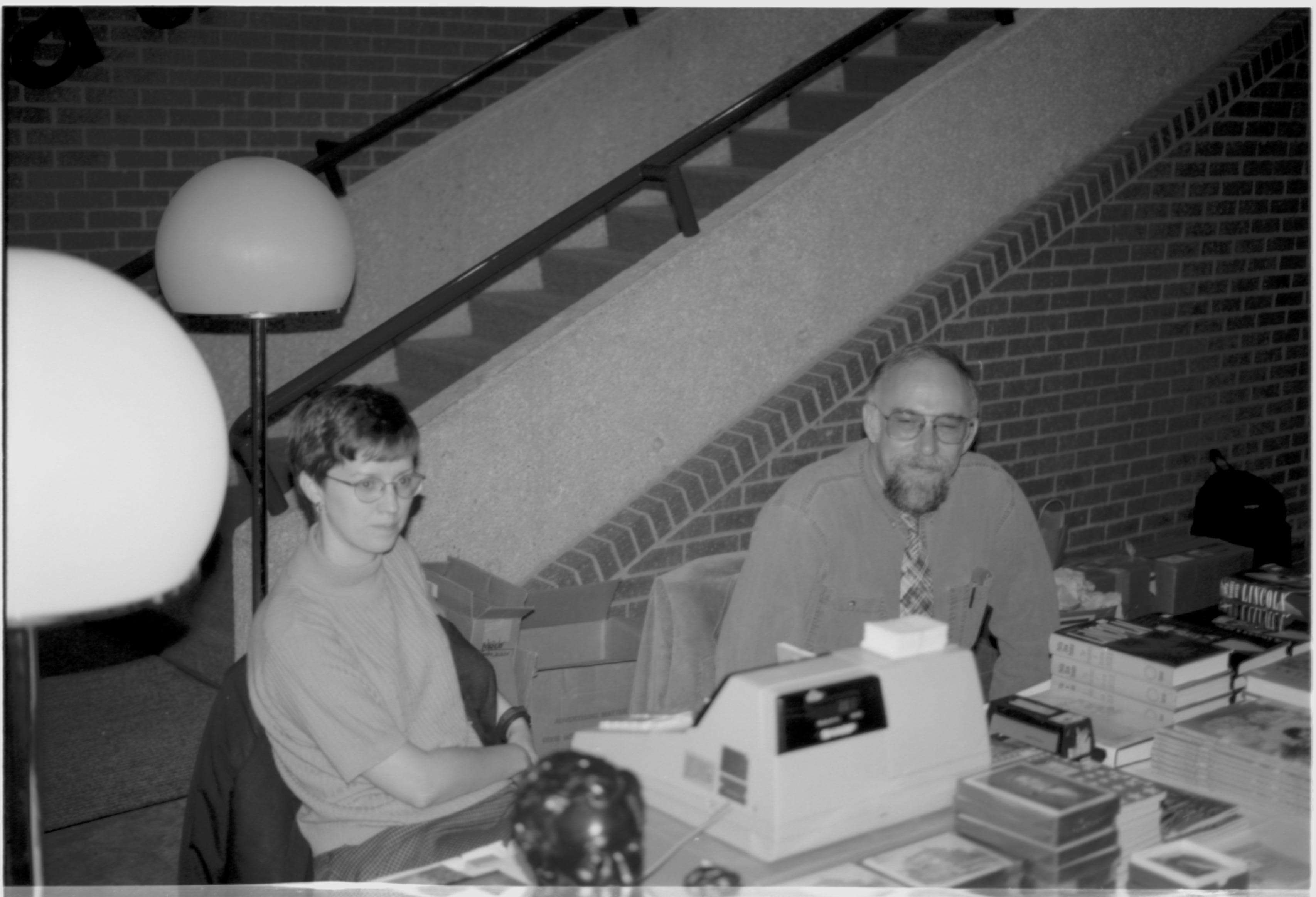 Two people sitting behind cash register. Lincoln Colloquium; UIS Roll#2, 4of4 Lincoln, Colloquium