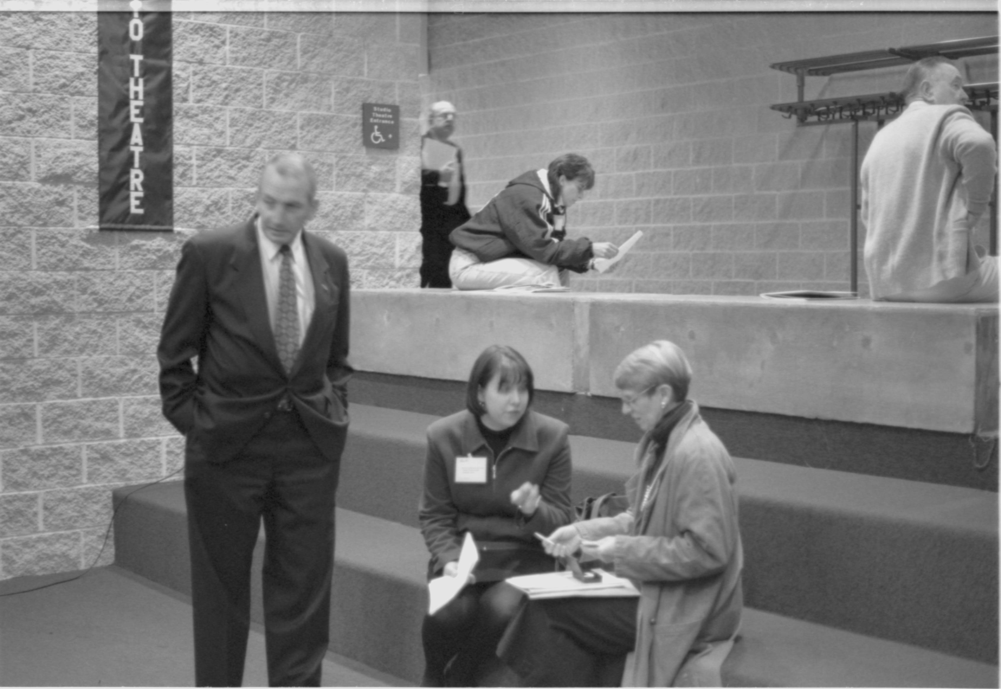 Man standing with hands in pockets, two ladies sitting. 1-1997 Colloq (b/w) Colloquium, 1997