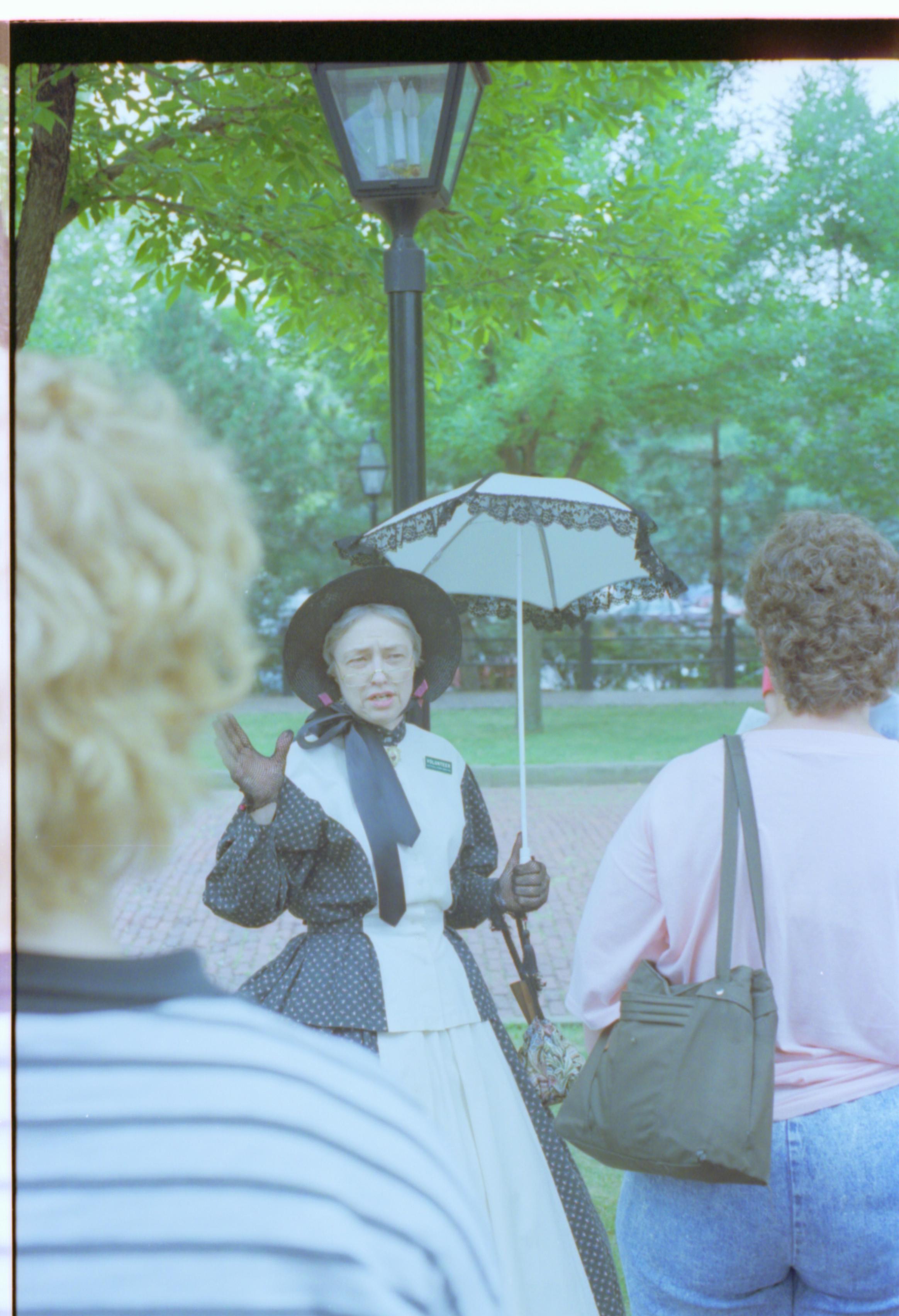Lady in period dress standing by light post. Interpretation