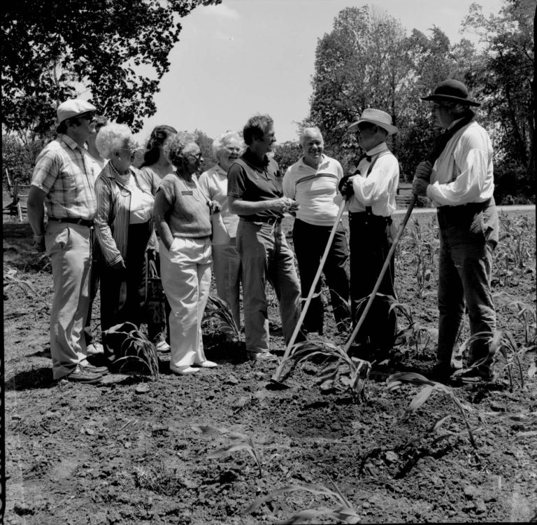 People in garden in period dress. Speaking to group. Log Cabin, State Park