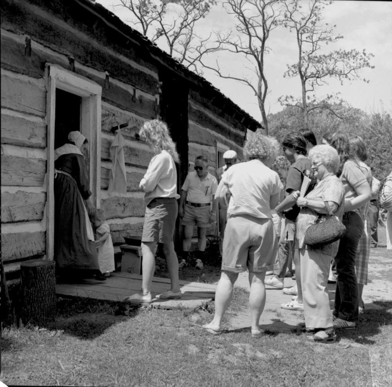 People standing outside log cabin. Log Cabin, State Park