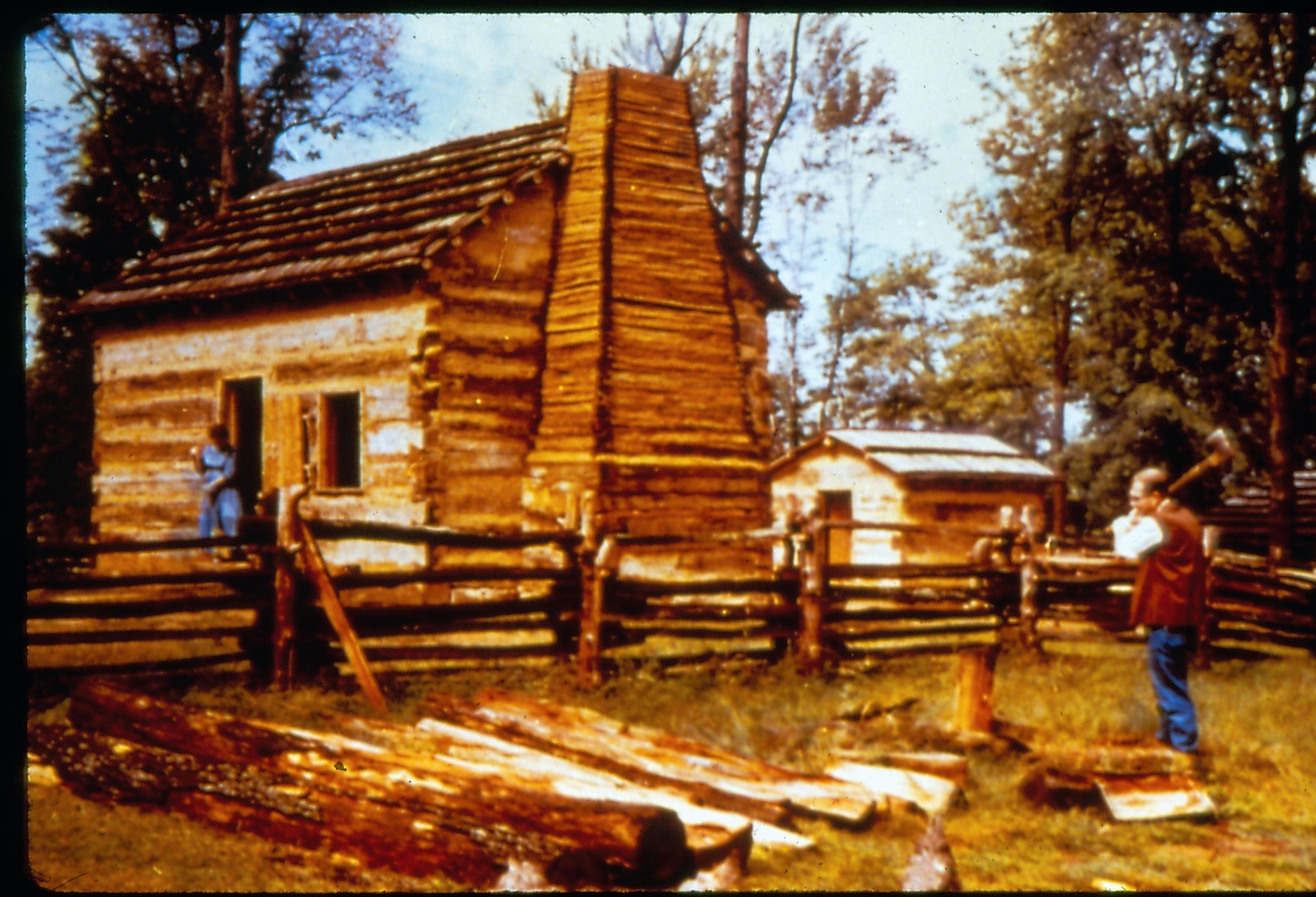 Log cabin & man in period dress splitting logs. New Salem