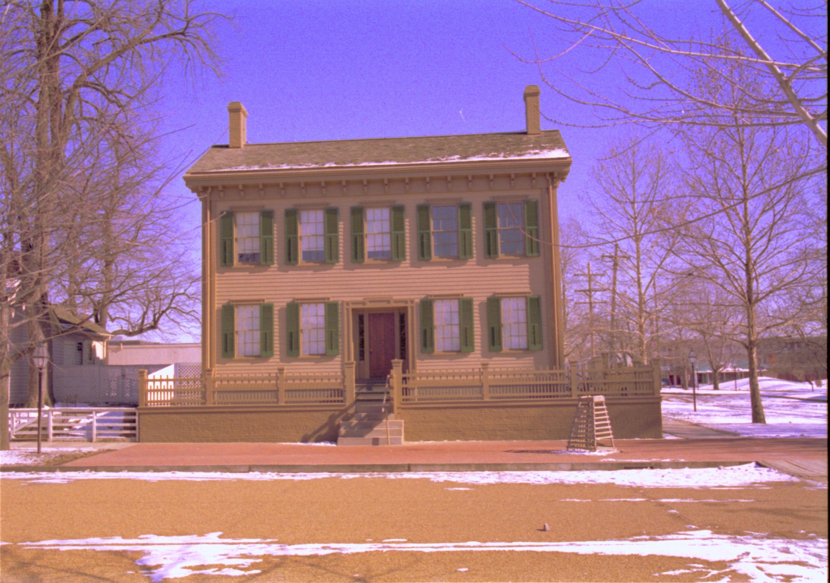 Lincoln Home in winter, snow scattered throughout, cleared brick plaza in front, elm tree in cage on right. Corneau House on left, B-2 in background left. Former Travel Lodge Motel in background right Looking East from west side of 8th Street snow, Lincoln Home, B-2, Travel Lodge Motel, 8th Street