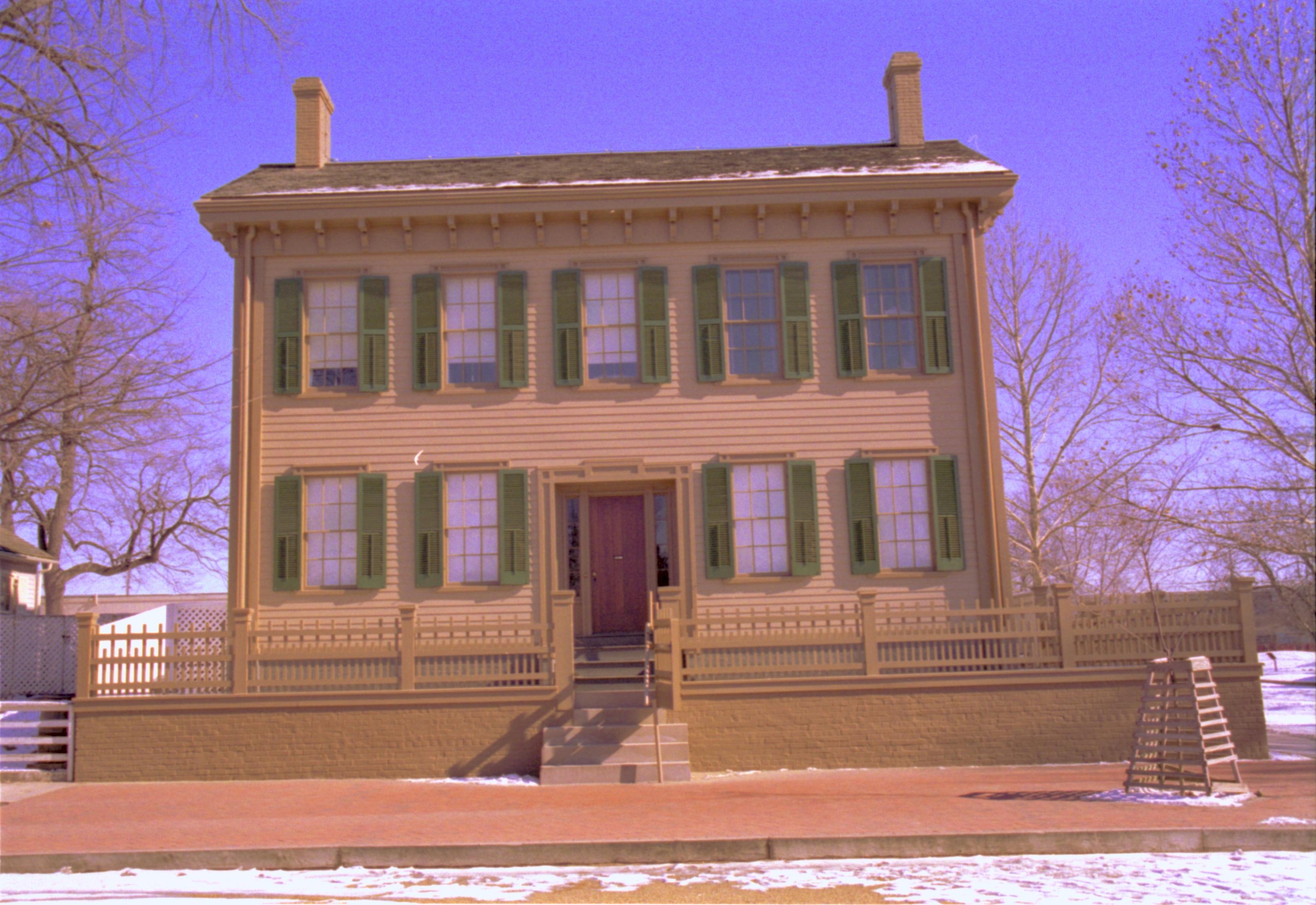 Lincoln Home in winter, snow scattered throughout. Cleared brick plaza in front, elm tree in cage on right. Corneau House on far left Looking East from 8th Street snow, Lincoln Home, brick plaza, Corneau, elm tree, 8th Street