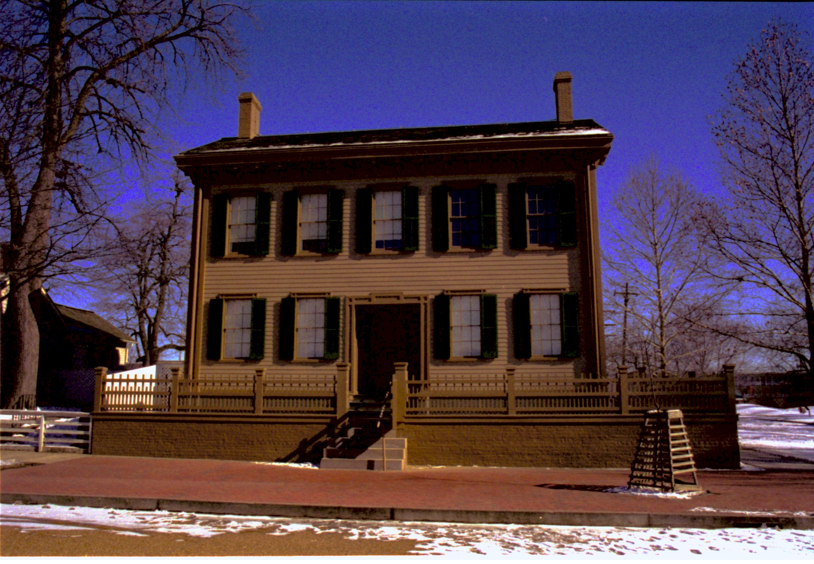 Lincoln Home in winter, some snow scattered throughout, cleared brick plaza in front, elm tree in cage on right.  Corneau House on left in shadow Looking Northeast from 8th Street snow, Lincoln Home, Corneau, brick plaza, 8th Street, elm tree