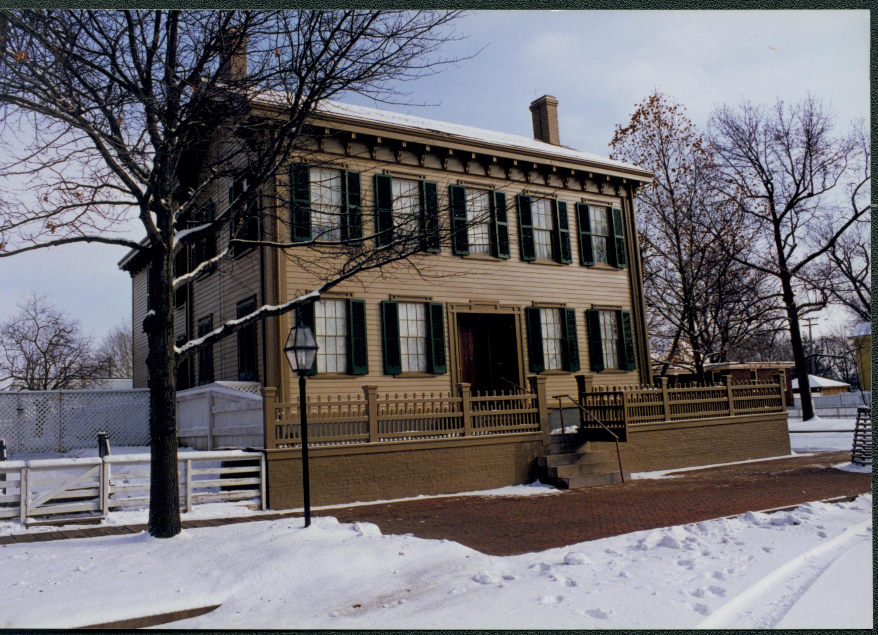 Lincoln Home in the snow with cleared brick plaza in front. Elm tree in cage on far right. Fence for Carrigan lot on left. Looking Southeast from 8th Street snow, Lincoln Home, 8th Street, brick plaza, elm tree