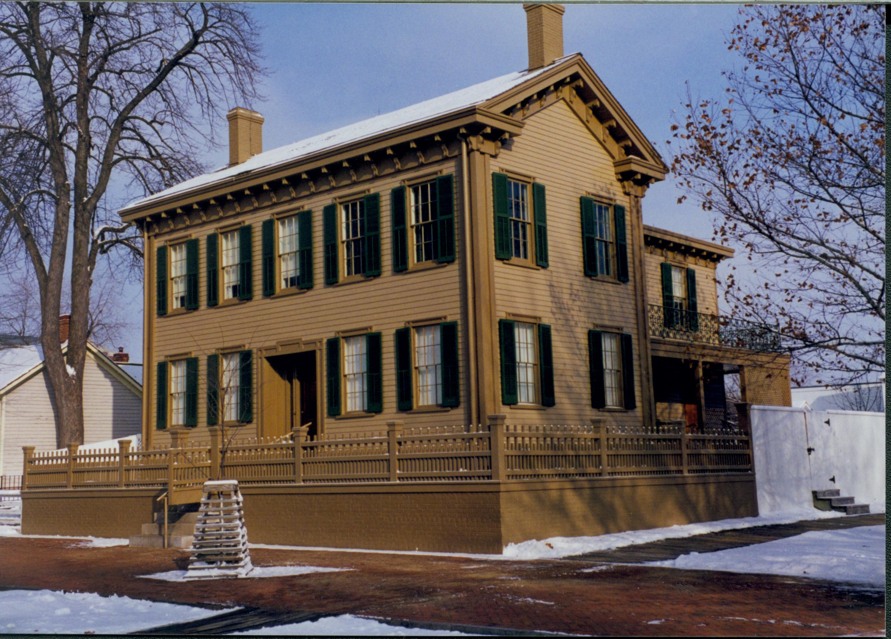 Lincoln Home in the snow with cleared brick plaza in front and cleared boardwalk along South side of house.  Elm tree in cage on plaza.  Corneau house on left. Looking Northeast from corner of 8th and Jackson Street intersection snow, Lincoln Home, brick plaza, elm tree, Corneau