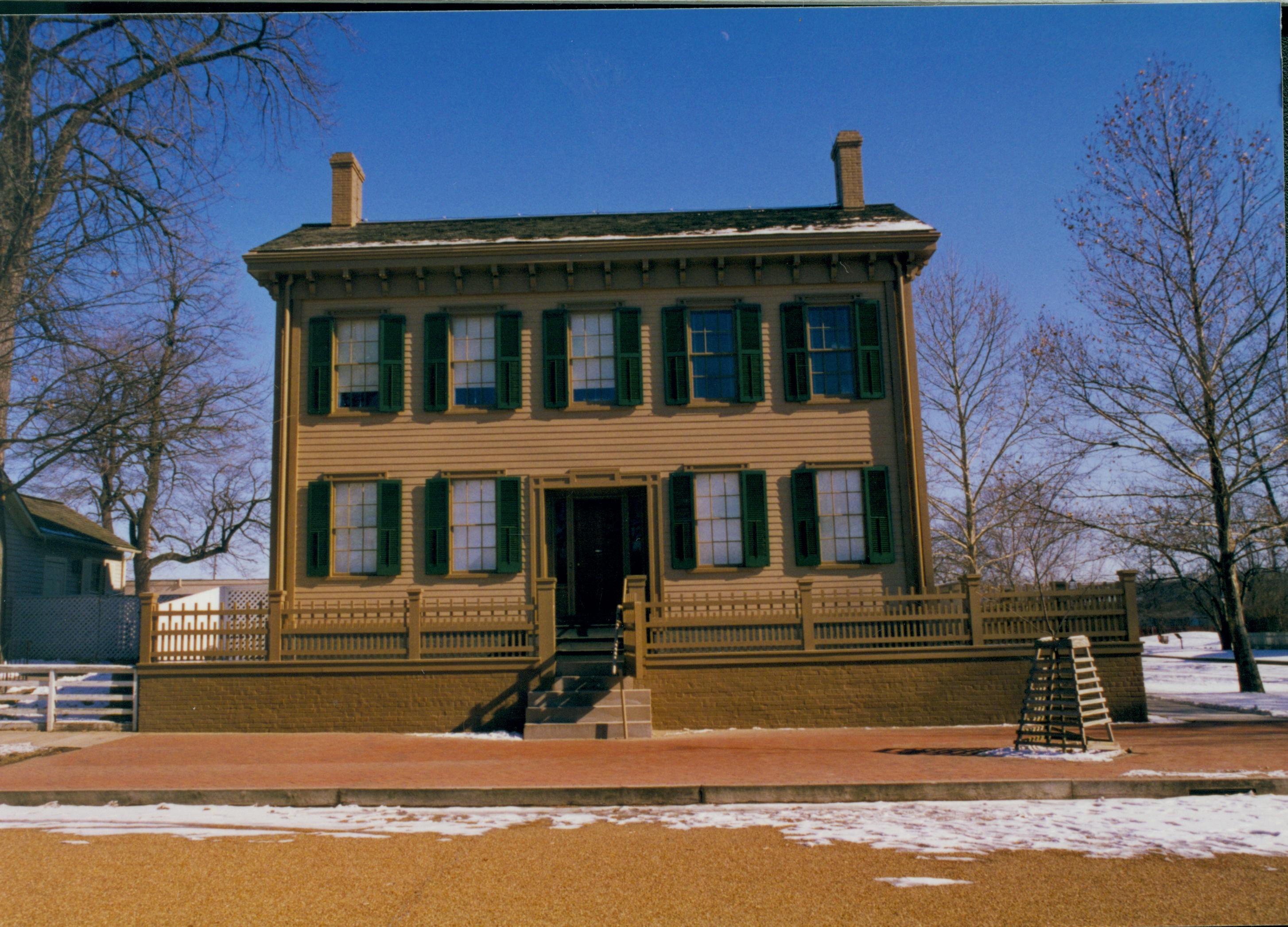 Lincoln Home in winter with some snow.  Cleared brick plaza in front with elm tree in cage on right.  Corneau House on left. Boardwalk visible on right Looking East from 8th Street snow, Lincoln Home, brick plaza, elm tree, 8th Street