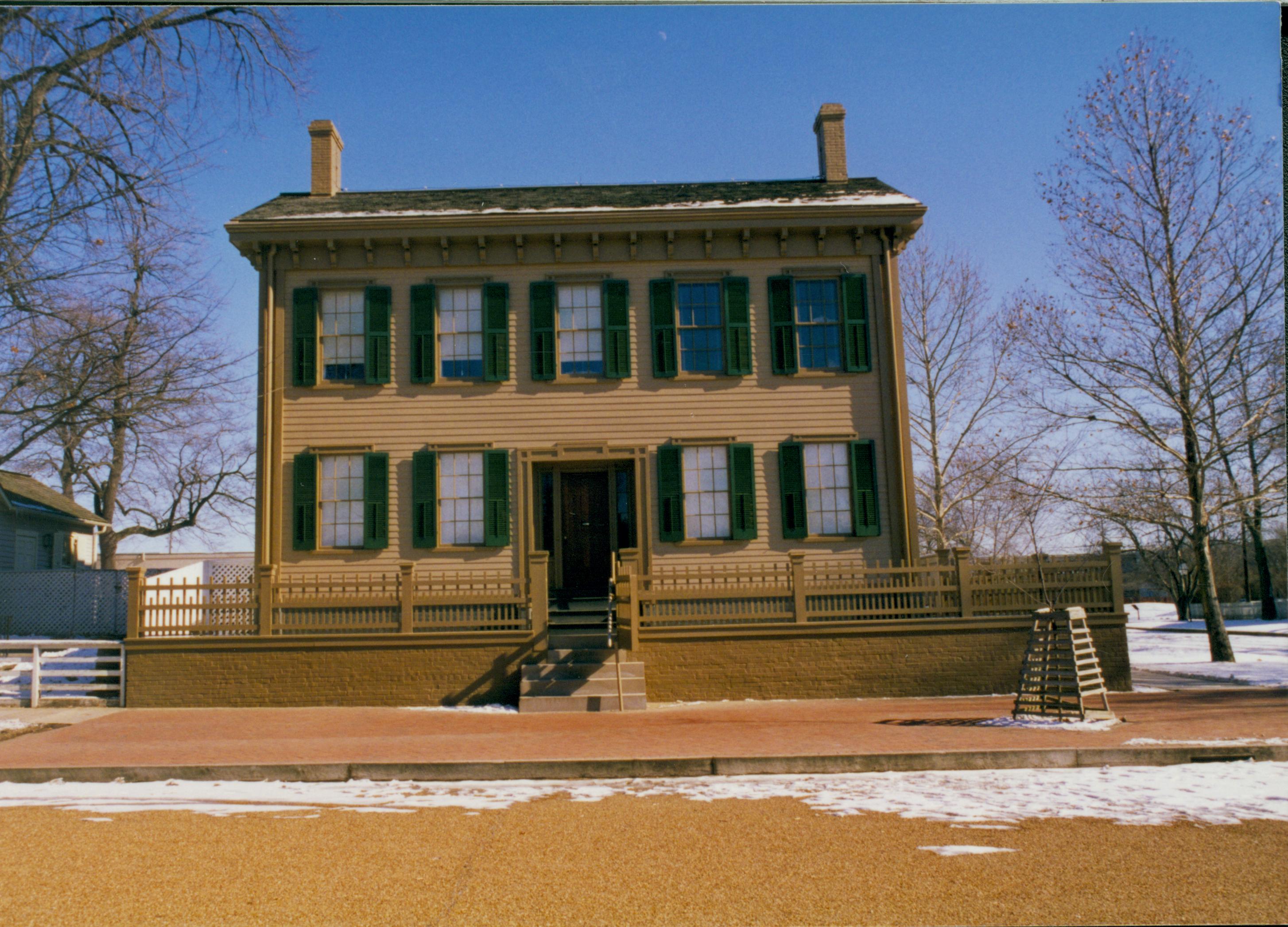 Lincoln Home in winter with some snow, cleared brick plaza in front, elm tree in cage on right.  Corneau House visible on left Looking East from 8th Street snow, Lincoln Home, Cornea, 8th Street, brick plaza, elm tree