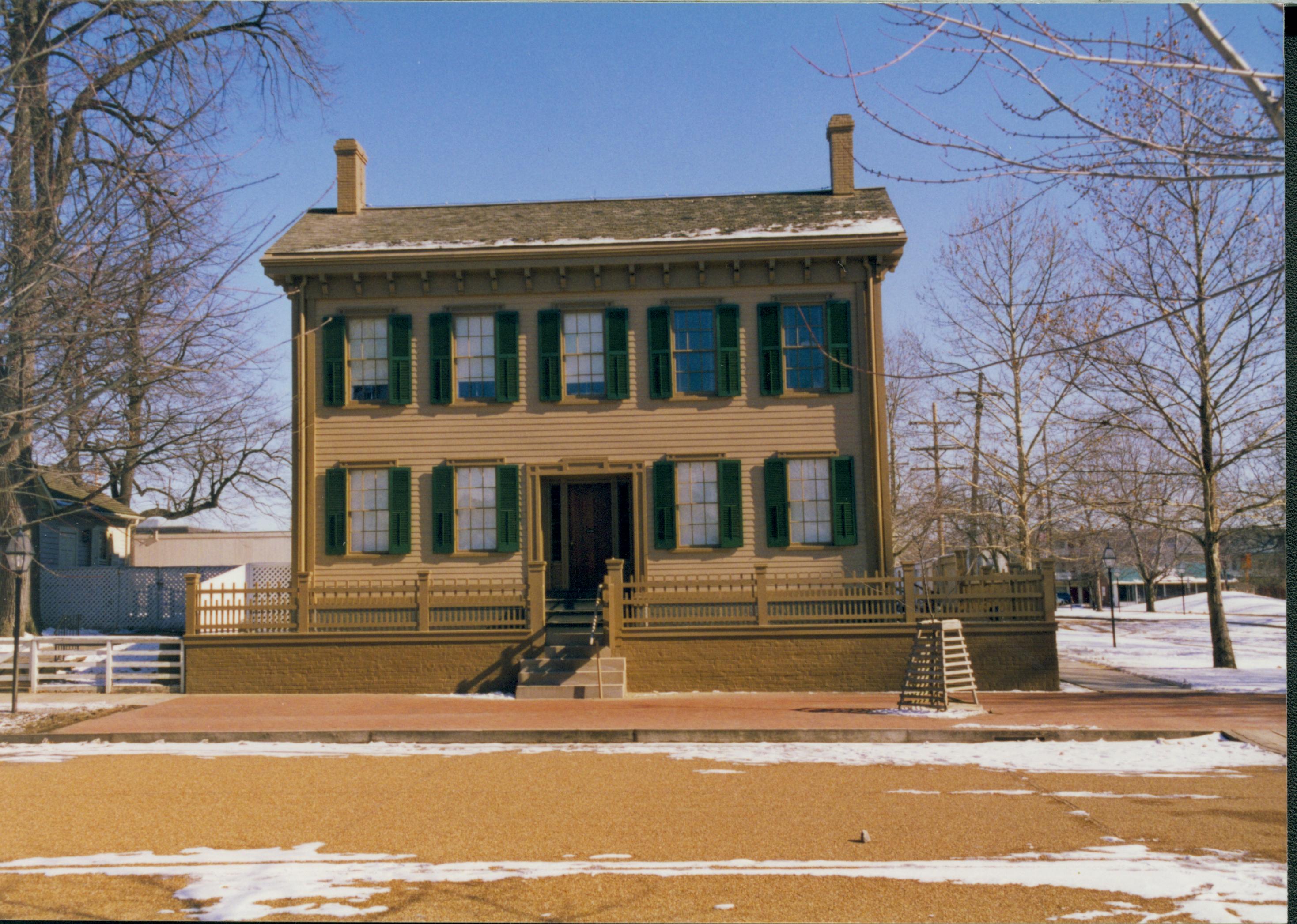 Lincoln Home in winter with some snow, cleared brick plaza in front, elm tree in cage on right. Corneau House on left with B-2 in between houses.  Cleared boardwalk on left. Looking East from west side of 8th Street snow, Lincoln Home, Corneau, B-2, brick plaza, elm tree, boardwalk