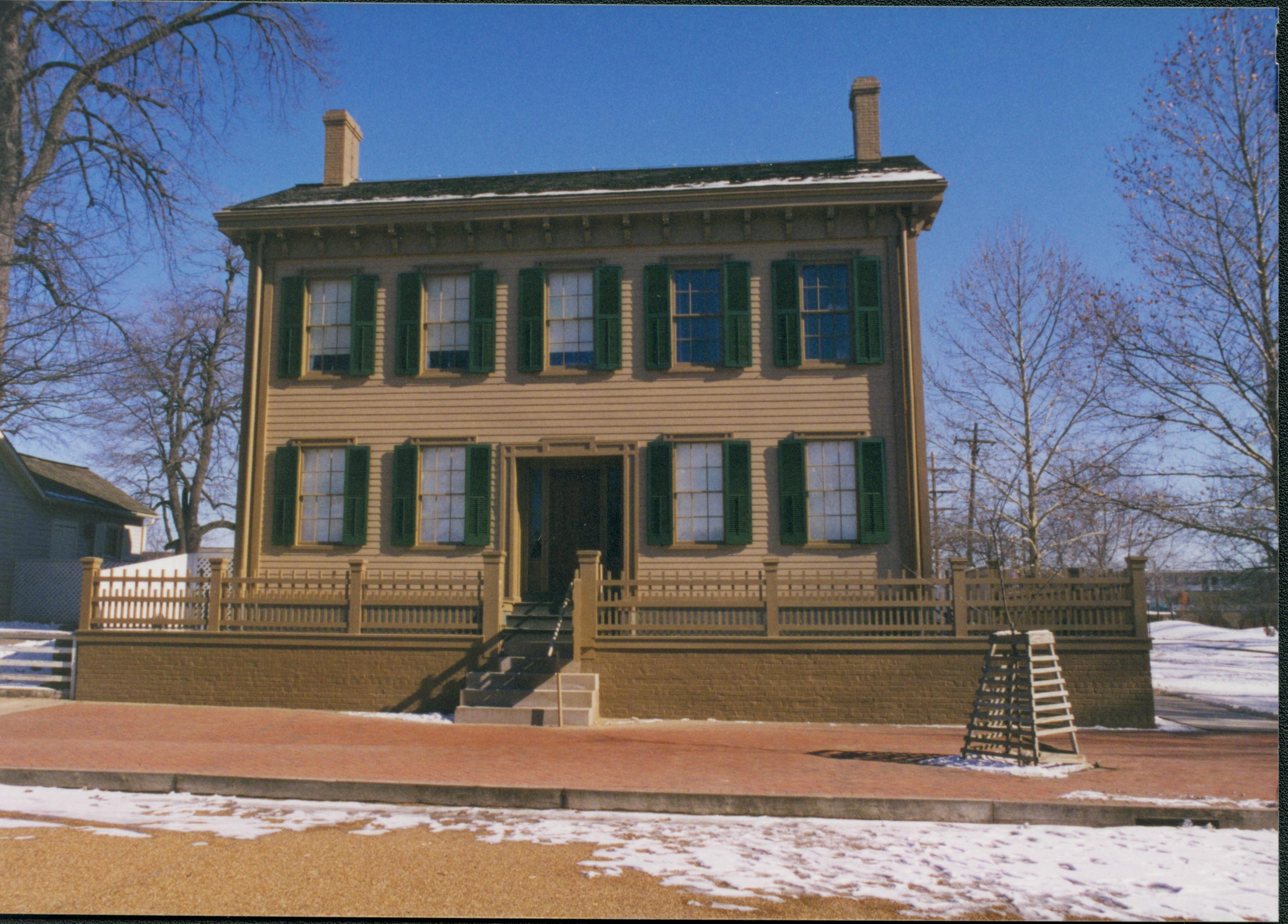 Lincoln Home in winter with some snow, cleared brick plaza in front, elm tree in cage on right. Corneau House on left. Cleared boardwalk on right. Looking East from 8th Street. snow, Lincoln Home, Corneau, brick plaza, elm tree, boardwalk, 8th Street