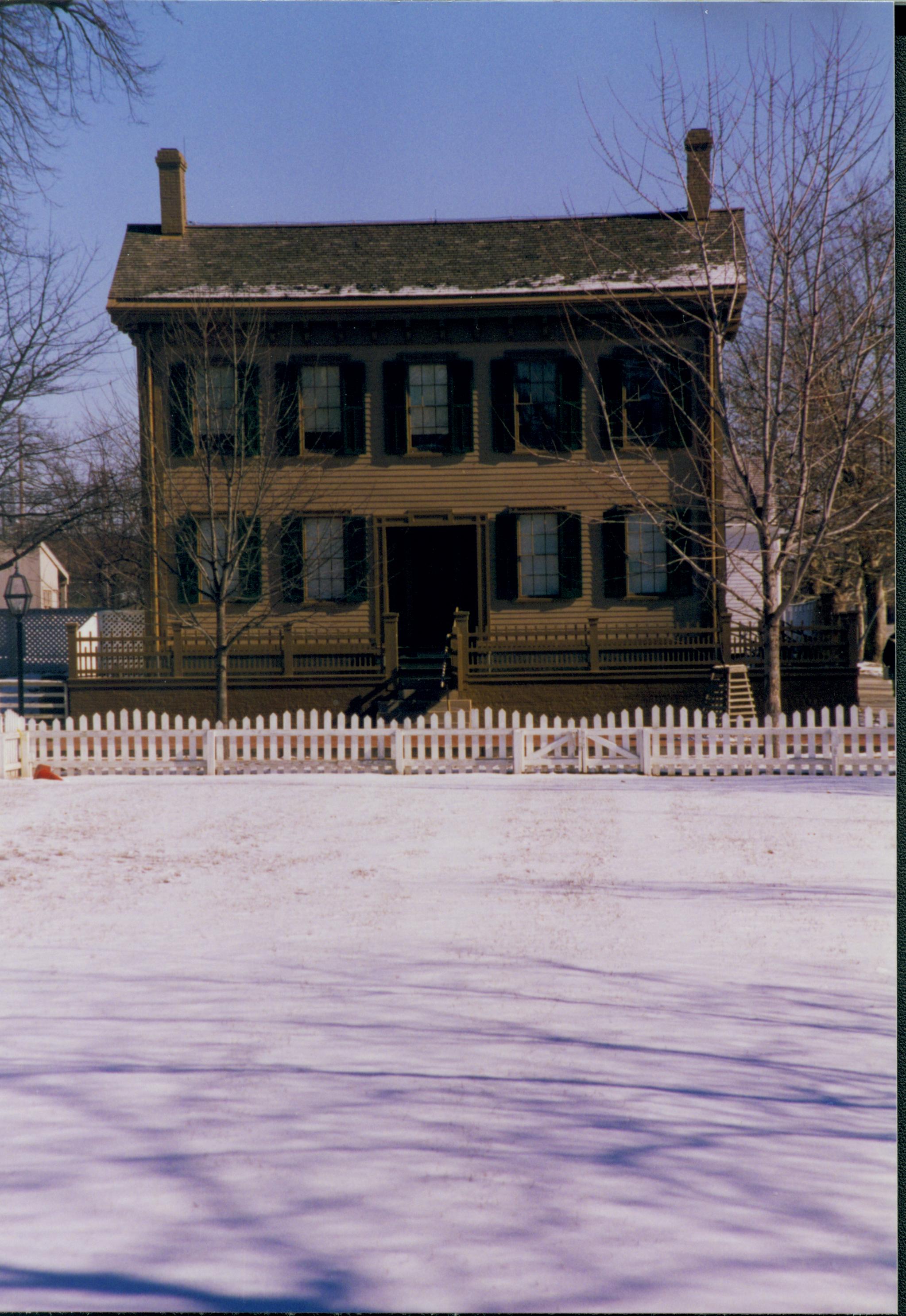 Lincoln Home in snow, from west end of Burch lot. B-2 in background on left. Lincoln Barn on right. Elm tree in cage on right. Fence in foreground surrounds Burch lot Looking East from Burch lot, Block 7, Lot 9 snow, Lincoln Home, Burch lot, B-2, elm tree