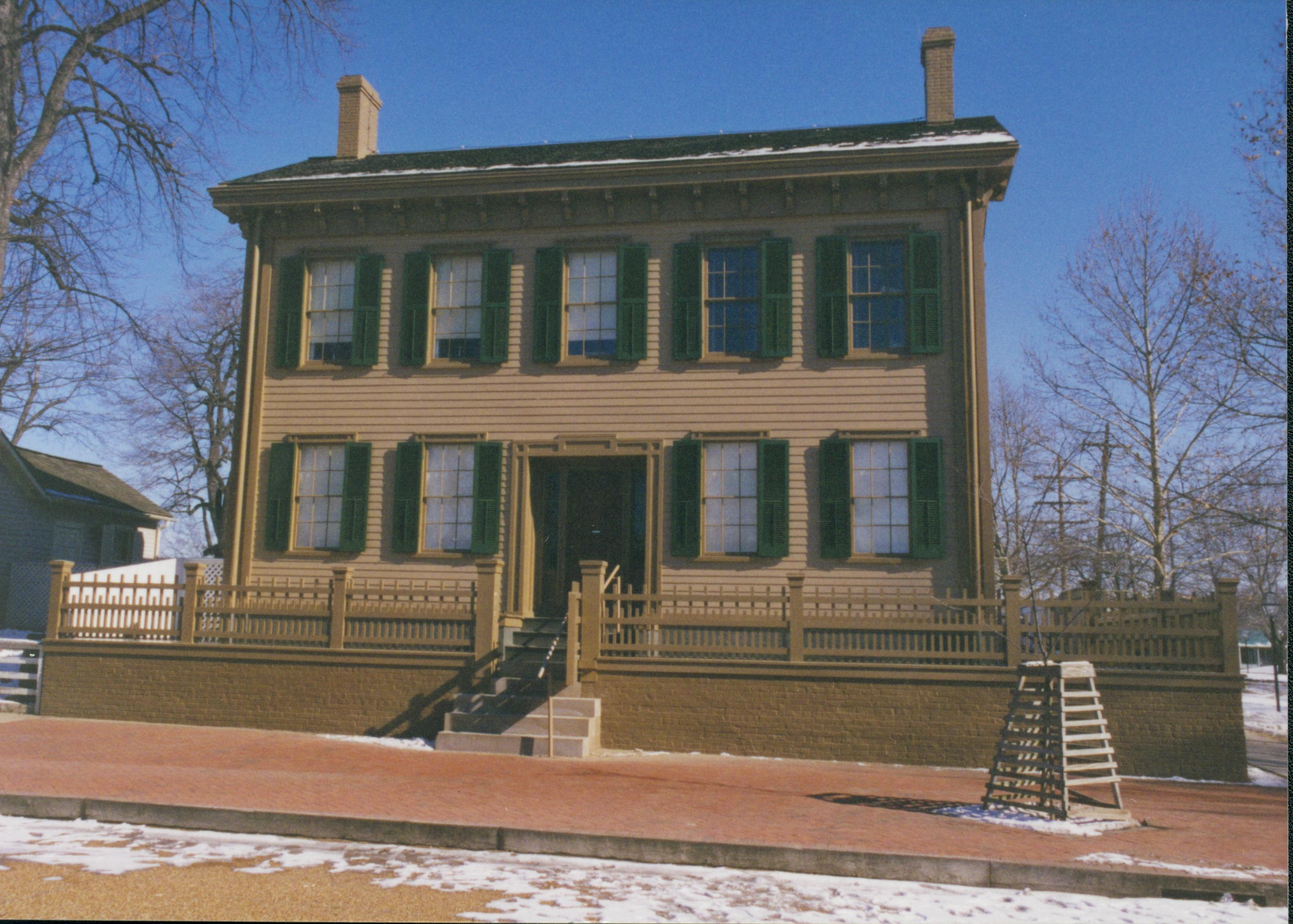 Lincoln Home in winter with some snow, cleared brick plaza in front, elm tree in cage on right. Corneau House on left. Looking East from 8th Street snow, Lincoln Home, brick plaza, elm tree, Corneau, 8th Street