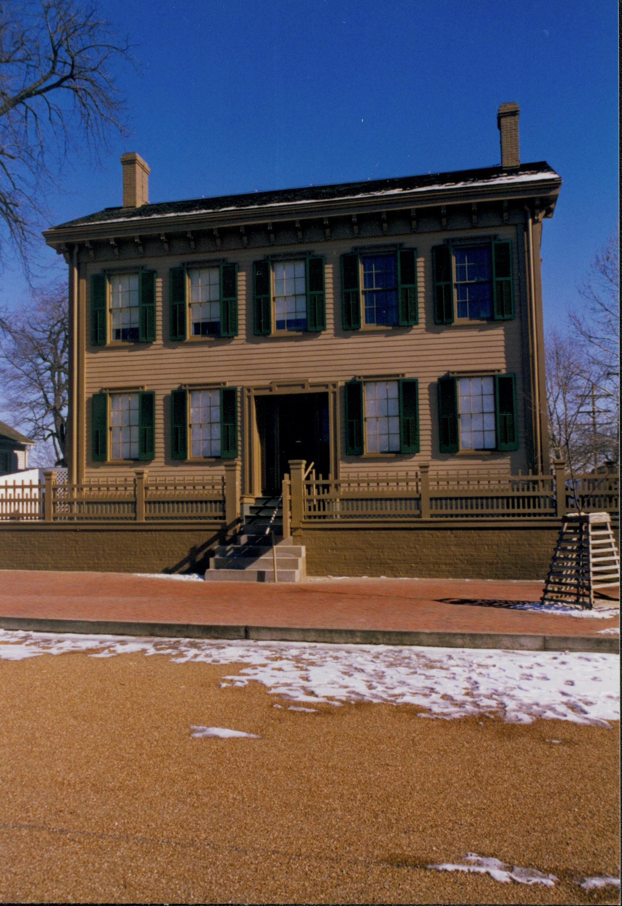 Lincoln Home in winter with some snow, cleared brick plaza in front, elm tree in cage on right. Corneau House on far left. Looking East from 8th Street snow, Lincoln Home, Corneau, 8th Street, brick plaza, elm tree