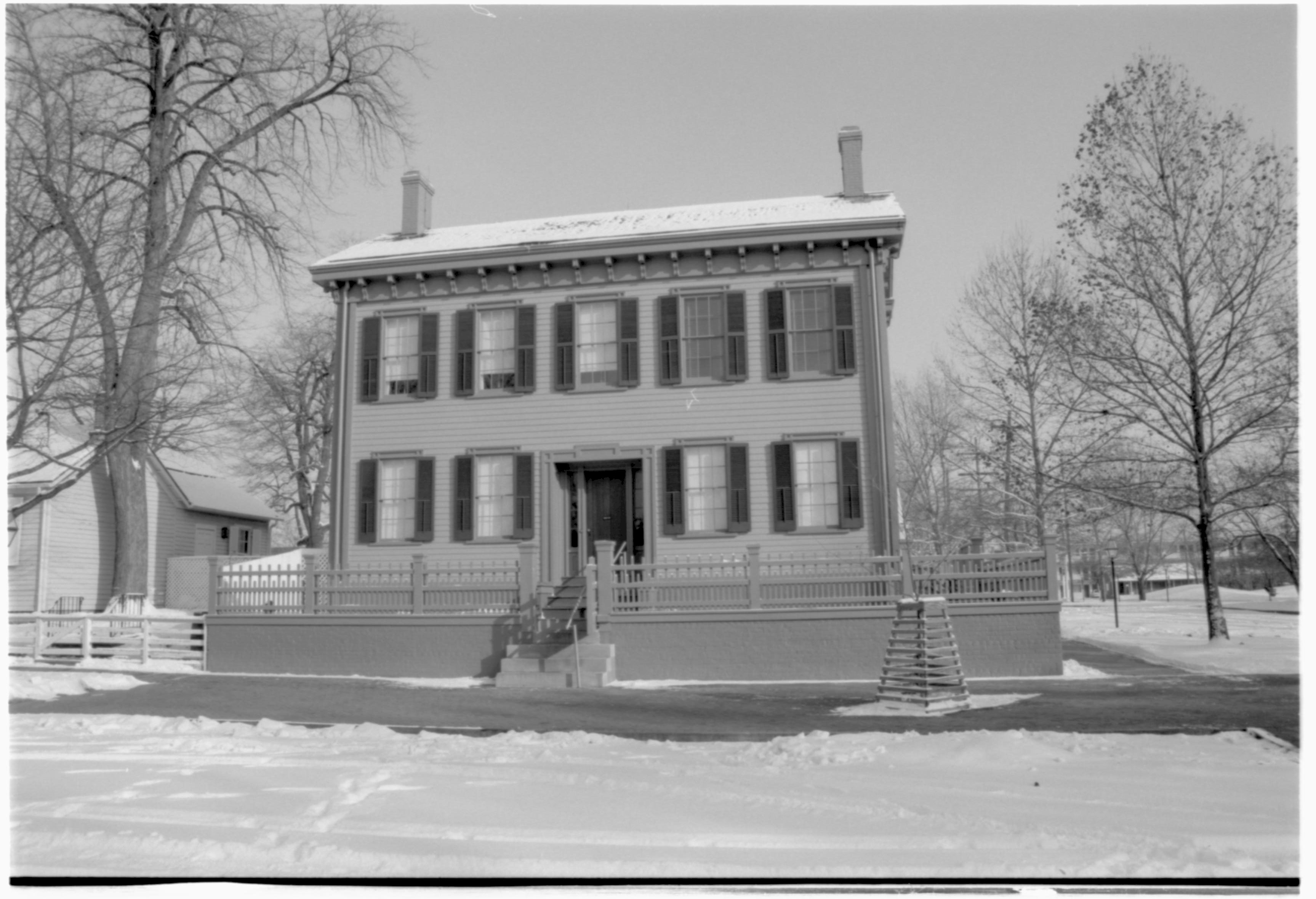 Lincoln Home in snow, cleared brick plaza in front, elm tree in cage on right, Corneau House on left. Cleared boardwalk on far right with former Travel Lodge Motel in far right background Looking East from 8th Street snow, Lincoln Home, Corneau, brick plaza, elm tree, 8th Street, Travel Lodge Motel