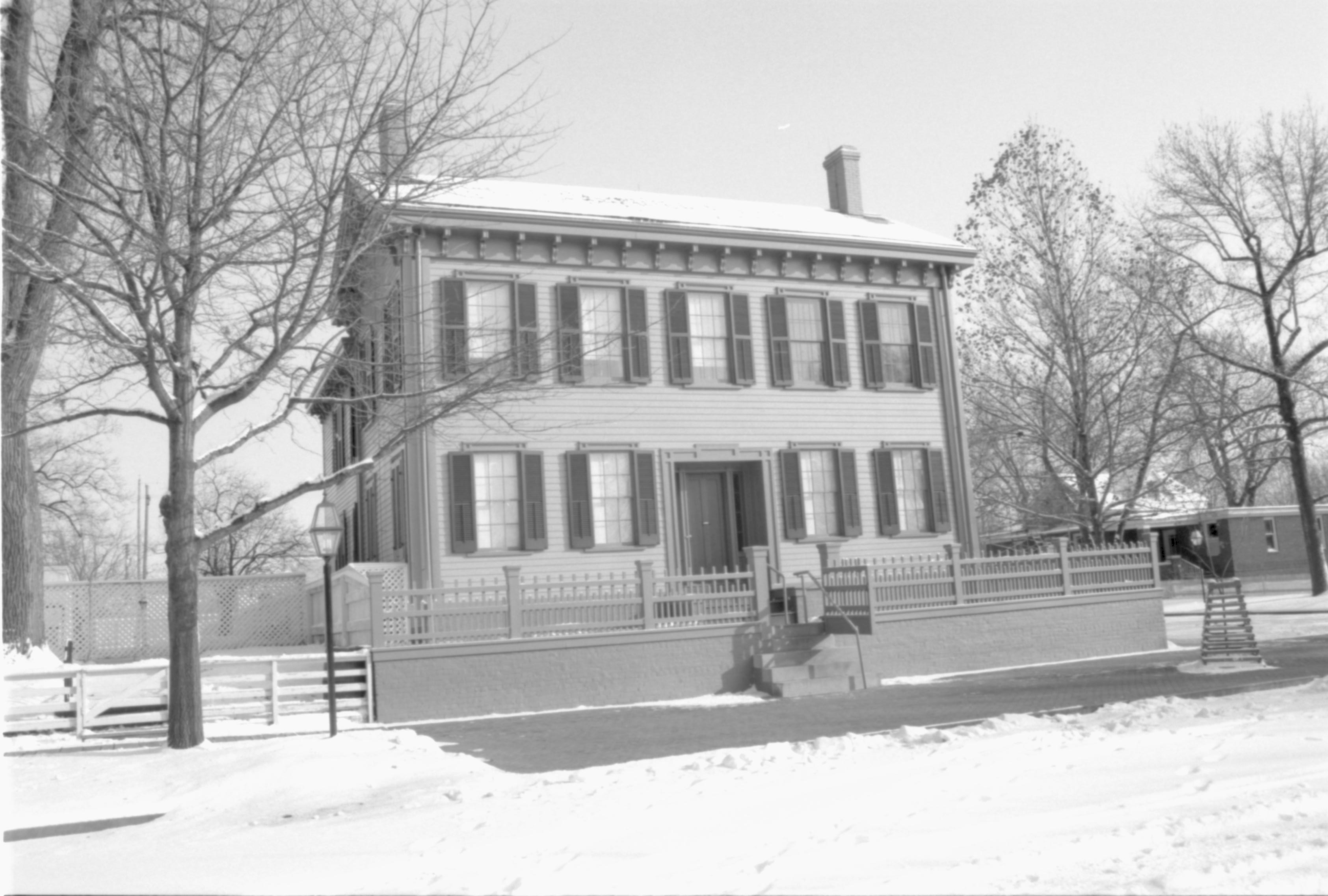 Lincoln Home in the snow, cleared brick plaza, elm tree in cage on right.  Arnold House in background right behind elm tree. Maintenance vehicle tracks and footprints in snow in foreground Looking Southeast from boardwalk on west side of 8th Street snow, Lincoln Home, Arnold, brick plaza, elm tree, 8th Street