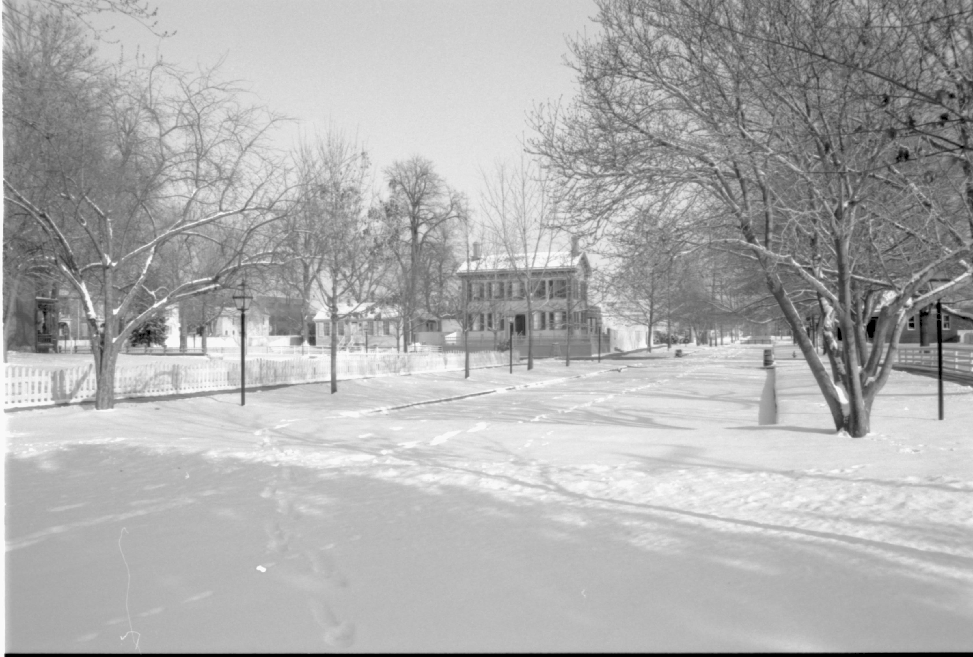 Lincoln neighborhood in the snow.  Lincoln Home in center, Corneau House on left, Morse House in background left, Dean House (dark building) and Conference Center in brick on far left.  Arnold House in background right.  Footprints visible in snow along Jackson Street. Looking Northeast from alley behind Visitor Center at intersection w/Jackson Street snow, Lincoln Home, Dean, Conference Center, Corneau, Arnold, Jackson Street, alley