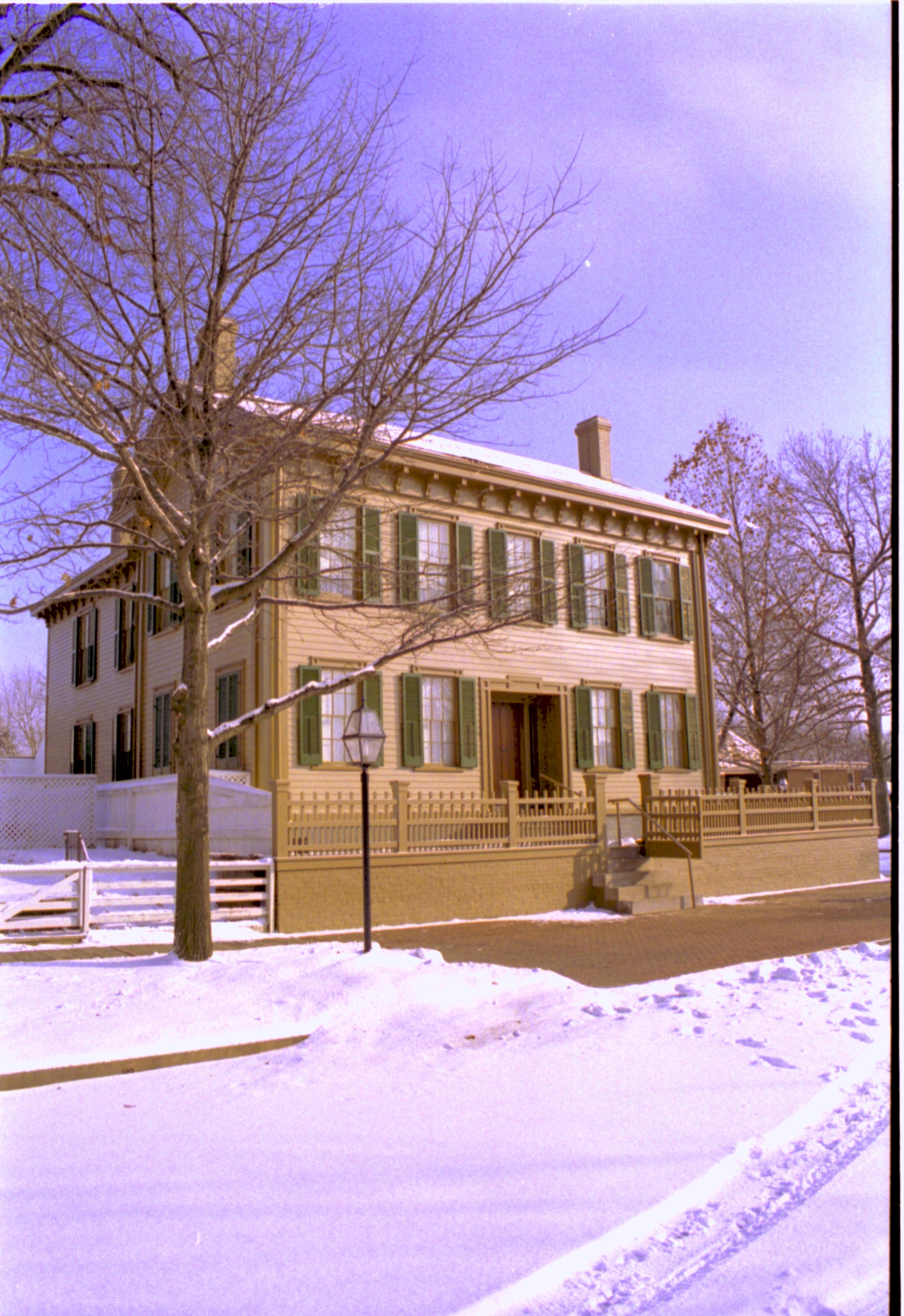 Lincoln Home in snow, cleared brick plaza in front. Arnold House just visible on right behind Lincoln Home picket fence. Maintenance vehicle tracks in snow in foreground Looking Southeast from 8th Street snow, Lincoln Home, Arnold, 8th Street