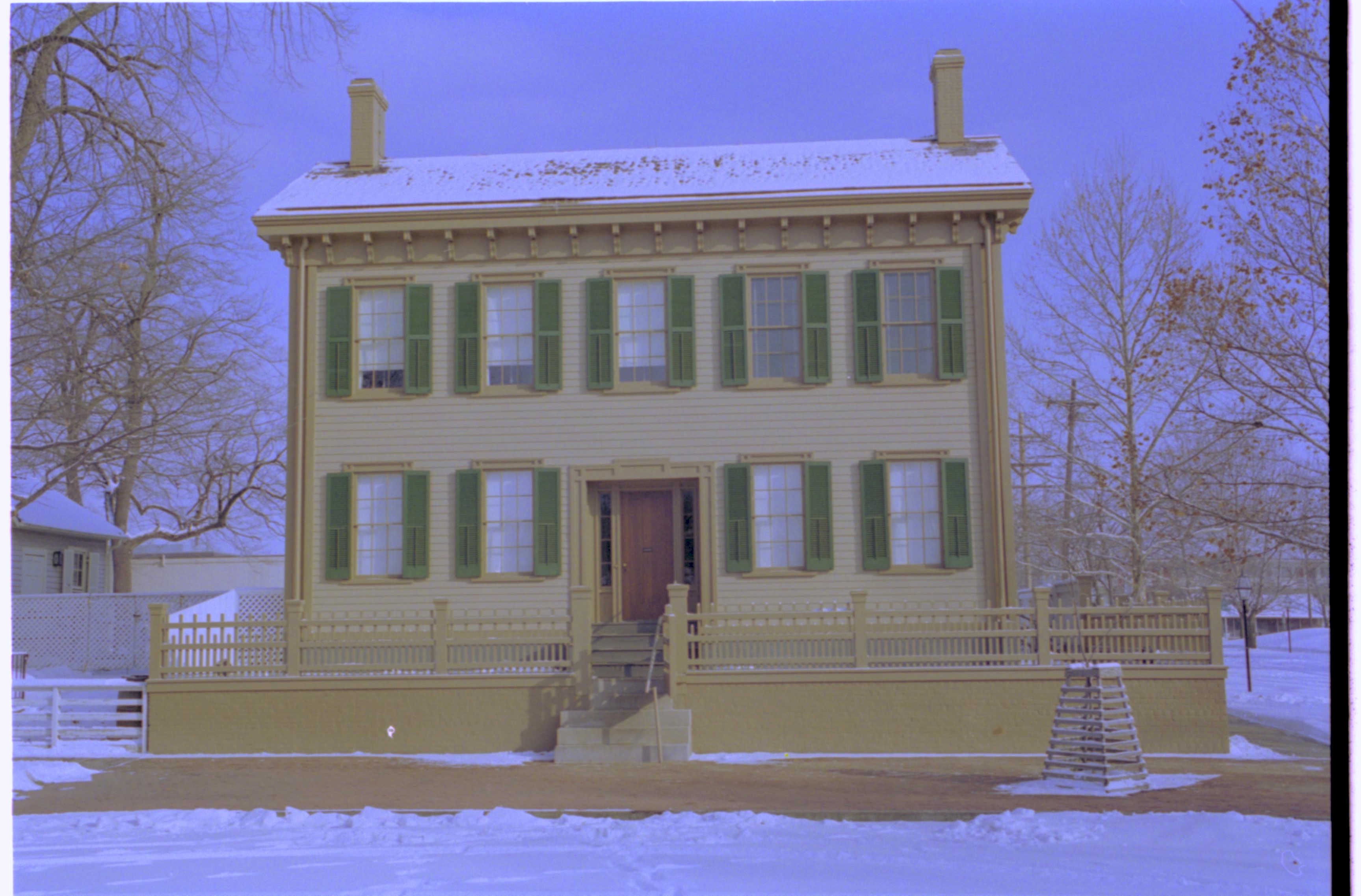 Lincoln Home in snow, cleared brick plaza in front, elm tree in cage on right. Corneau House on far left, B-2 in background left. Former Travel Lodge Motel in background right. Looking East from 8th Street snow, Lincoln Home, Corneau, B-2, Travel Lodge Motel, brick plaza, elm tree