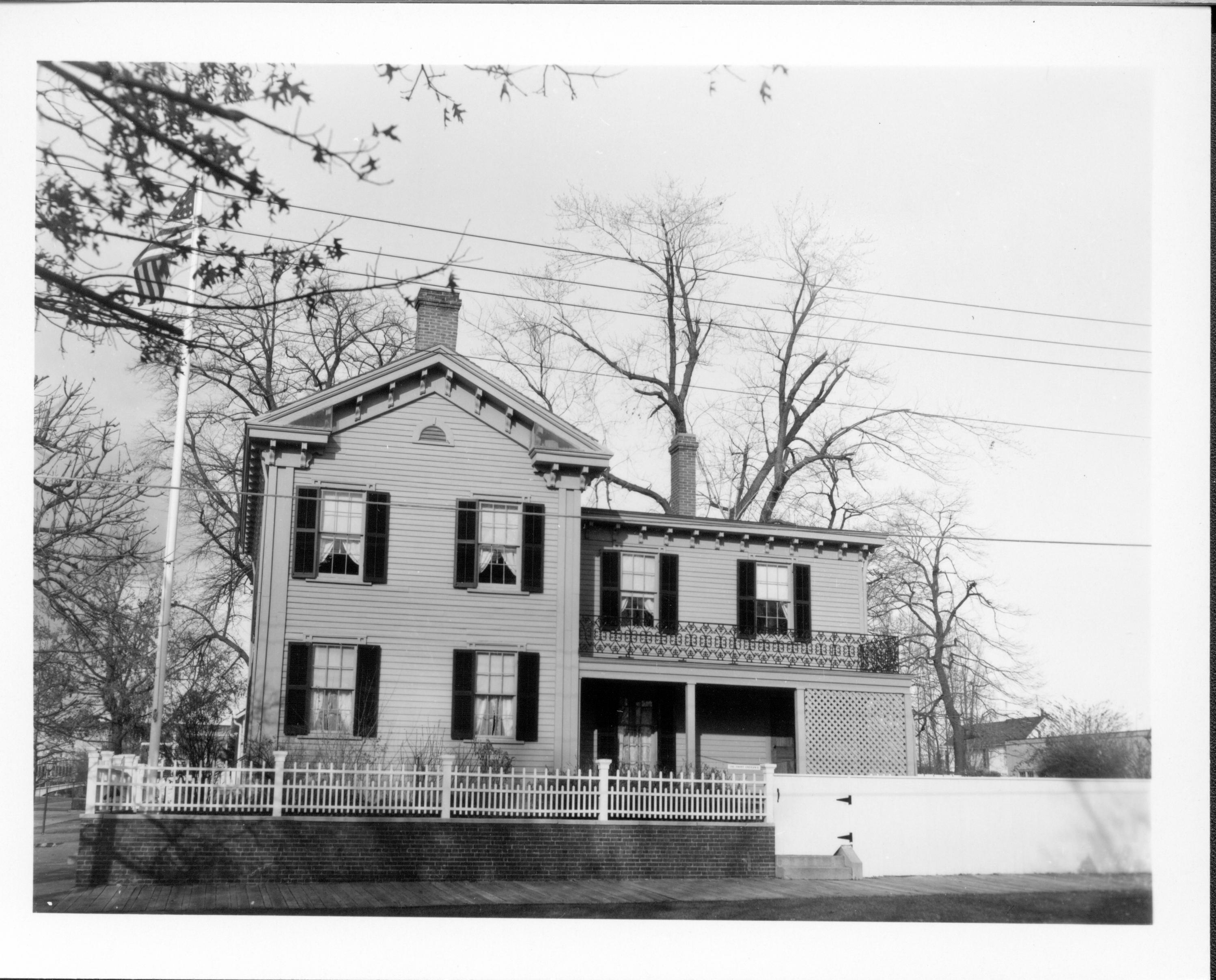 Lincoln Home - South elevation with flagpole behind the fence on the corner. B-2 visible behind the white fence in background right. Morse House (?) in far background right. Looking north from Jackson Street Lincoln Home, fences, flagpole, B-2, Morse, Jackson Street, utility lines