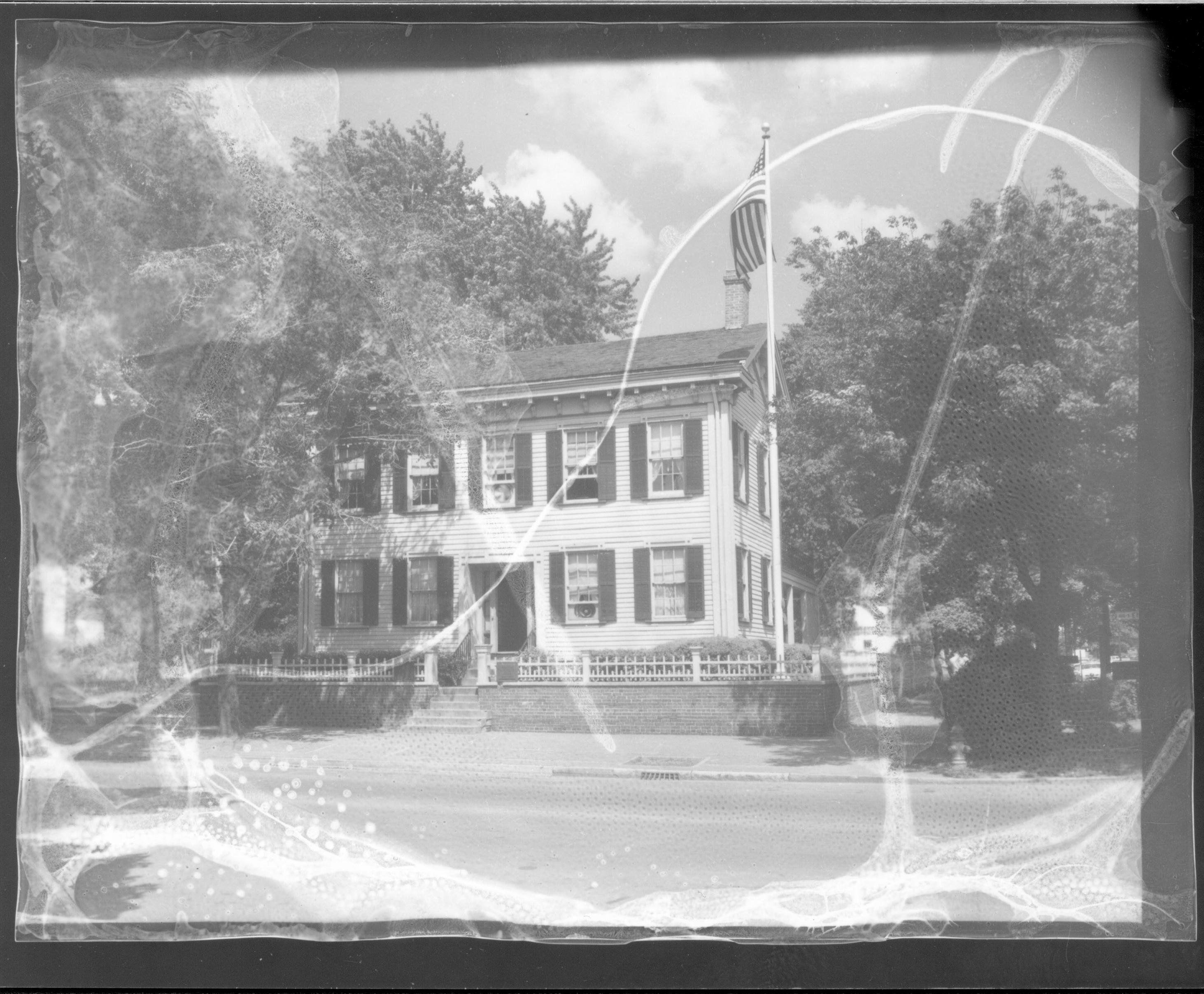 Lincoln Home west (front) elevation in summer surrounded by trees. Flagpole on corner behind picket fence, fire hydrant visible on corner near street. Two-story houses visible on far left and behind Lincoln Home. House appears to be painted white. Looking East/Northeast from 8th and Jackson Street intersection. Negative deteriorating Lincoln Home, flagpole, fire hydrant, 8th Street, painted white, summer