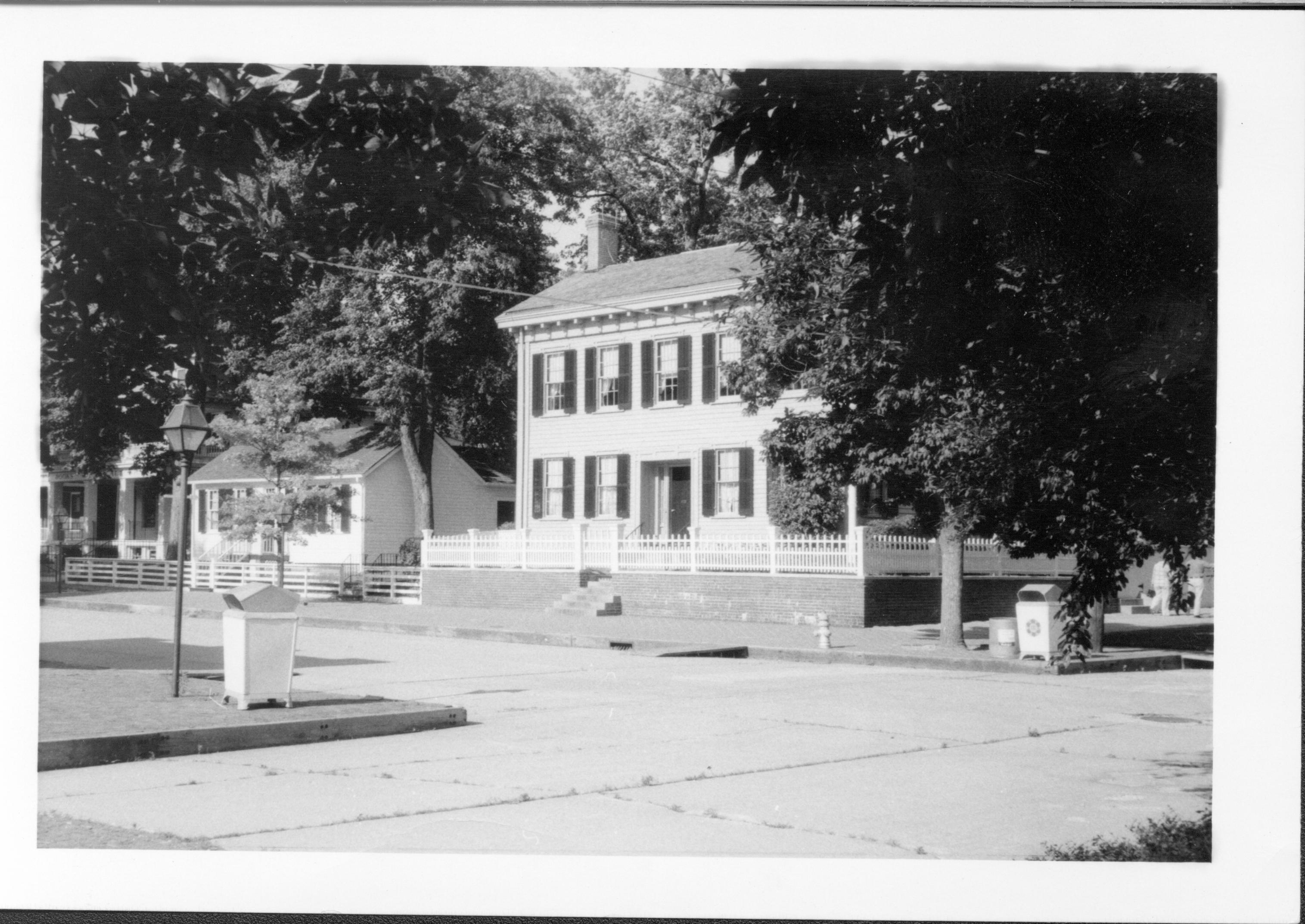 Lincoln Home from 8th and Jackson Street intersection. Corneau House on left, two-story house on Bugg lot (Block 10, Lot 5) on far left. Concrete streets, trash cans on corners, fire hydrant near street in front of Lincoln Home. Ramps leading to street. House appears to be painted white Looking Northeast Lincoln Home, Corneau, Bugg, ramps, summer, fire hydrant, painted white (?)