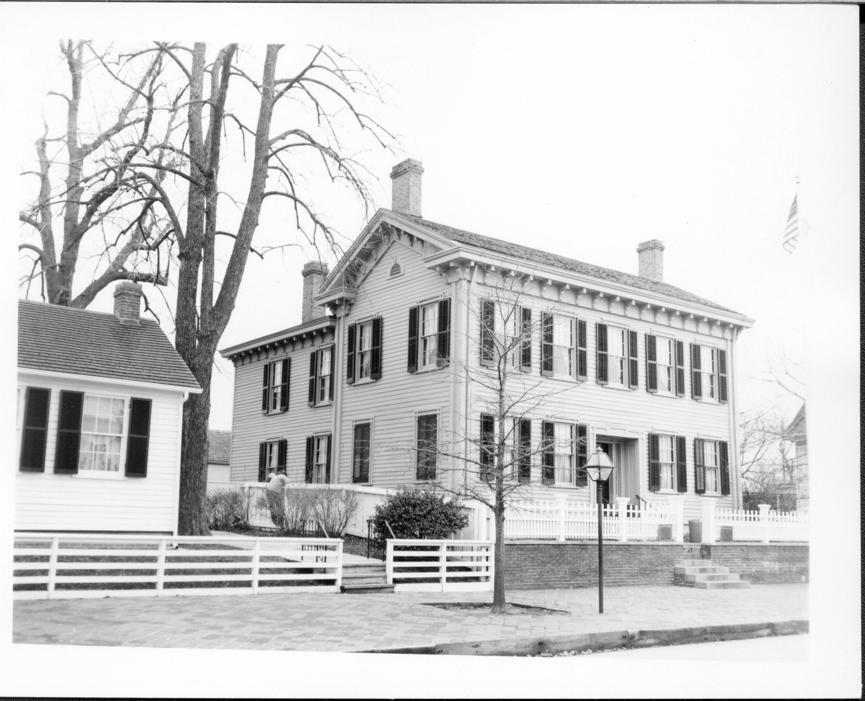 Lincoln Home west (front) elevation. Corneau House on left. Rebecca Cook house on far right. Person hanging on fence between Corneau & Lincoln Home. Lincoln Barn visible between houses also. Flagpole on corner in far right Looking Southeast from 8th Street Lincoln Home, Corneau, Rebecca Cook, flagpole, Lincoln Barn, staff(?)