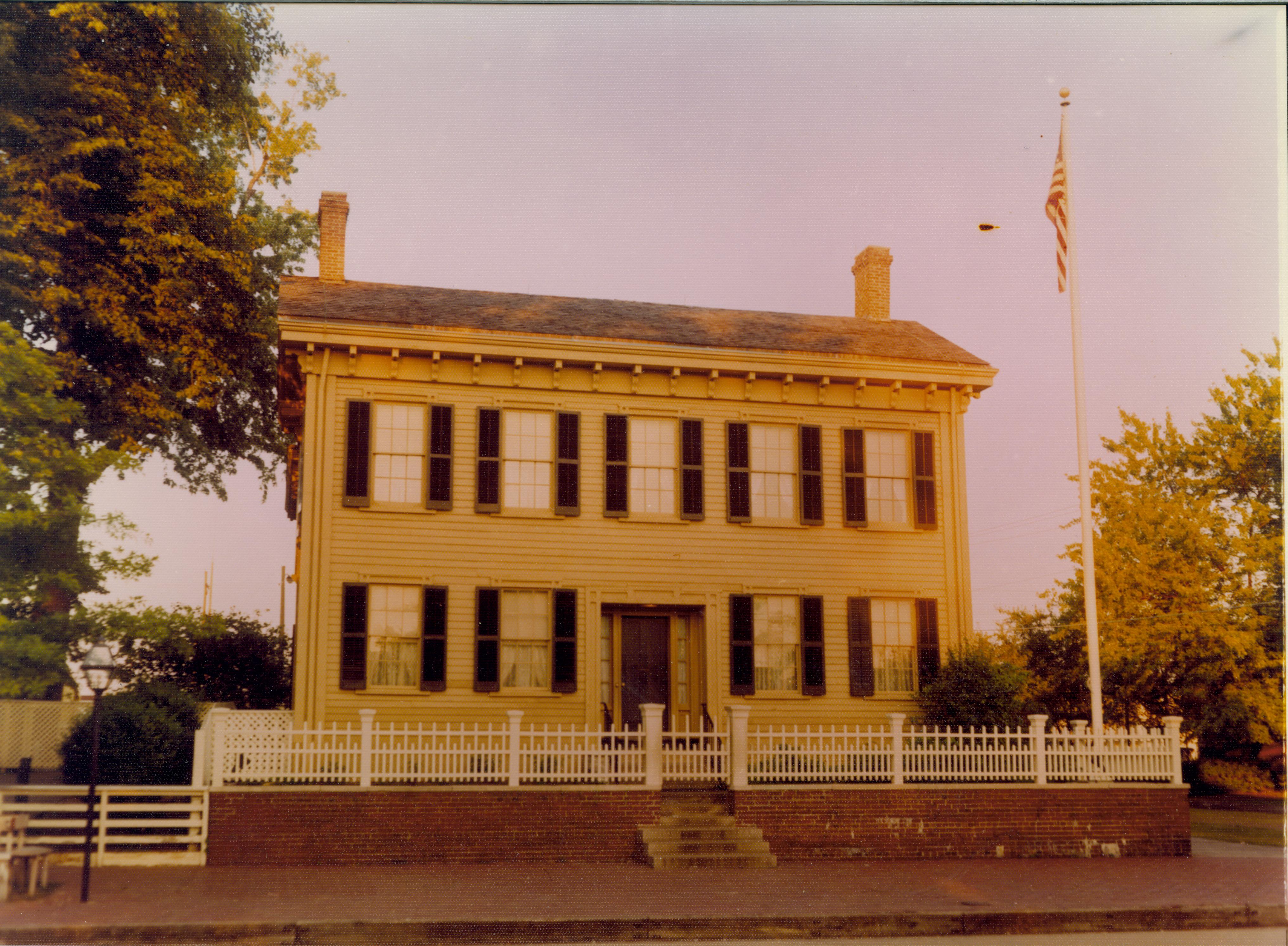 Lincoln Home west (front) elevation. Flagpole on right corner behind picket fence, utility poles in background left  Looking east from 8th Street Lincoln Home, summer, flagpole