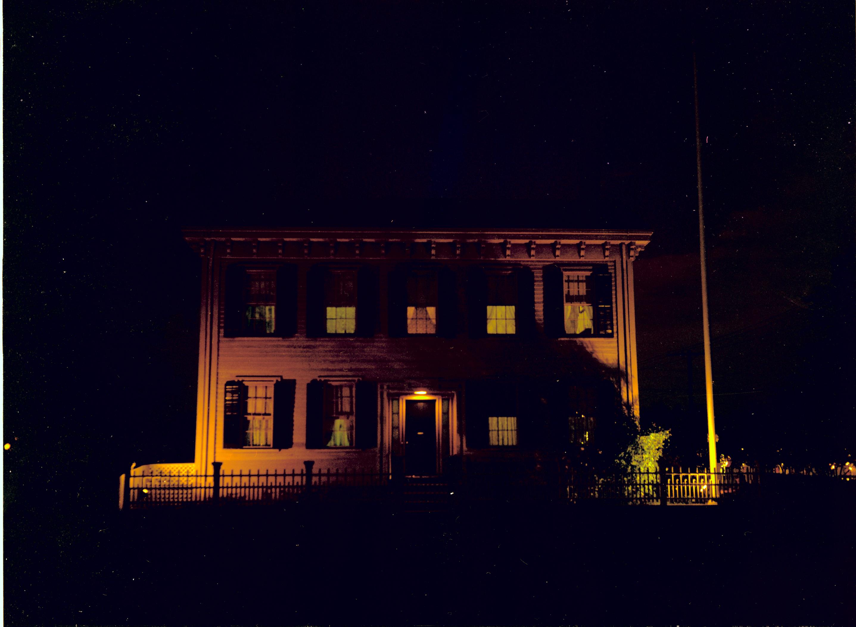 Lincoln Home west (front) elevation at night. Lighted flagpole on corner behind picket fence on right. Lights on inside house. Looking East from 8th Street Lincoln Home, night, 8th Street, flagpole