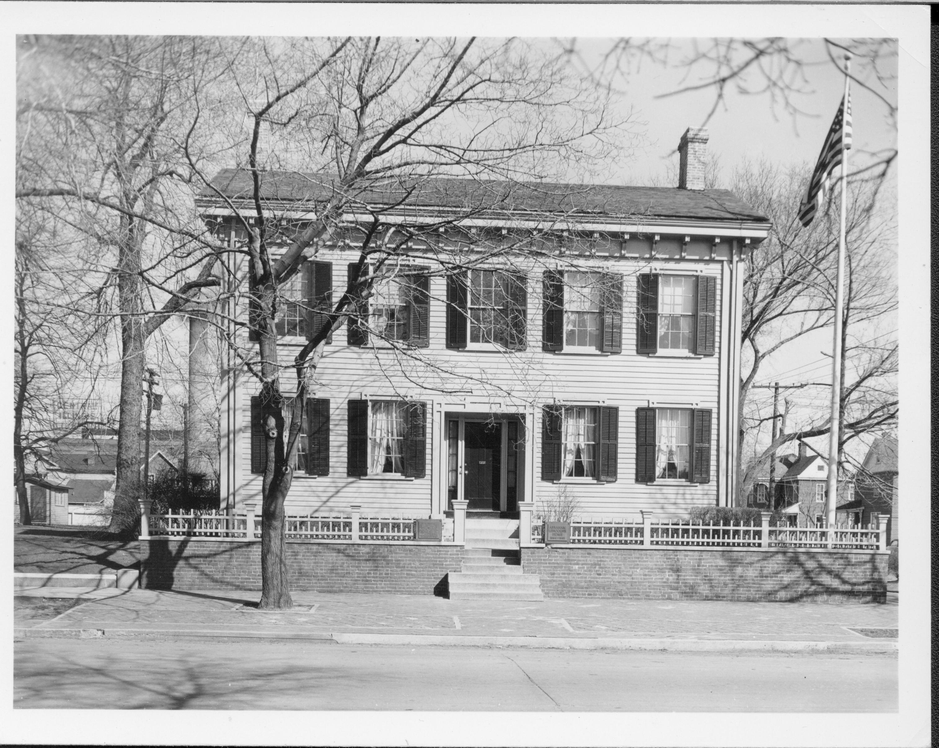 Lincoln Home west (front) elevation, flagpole in corner behind picket fence on right.  Several homes visible behind Lincoln Home on Blocks 10 and 11.  Large tree in brick plaza on left. Looking East from 8th Street Lincoln Home, flagpole, 8th Street, Block 10, Block 11