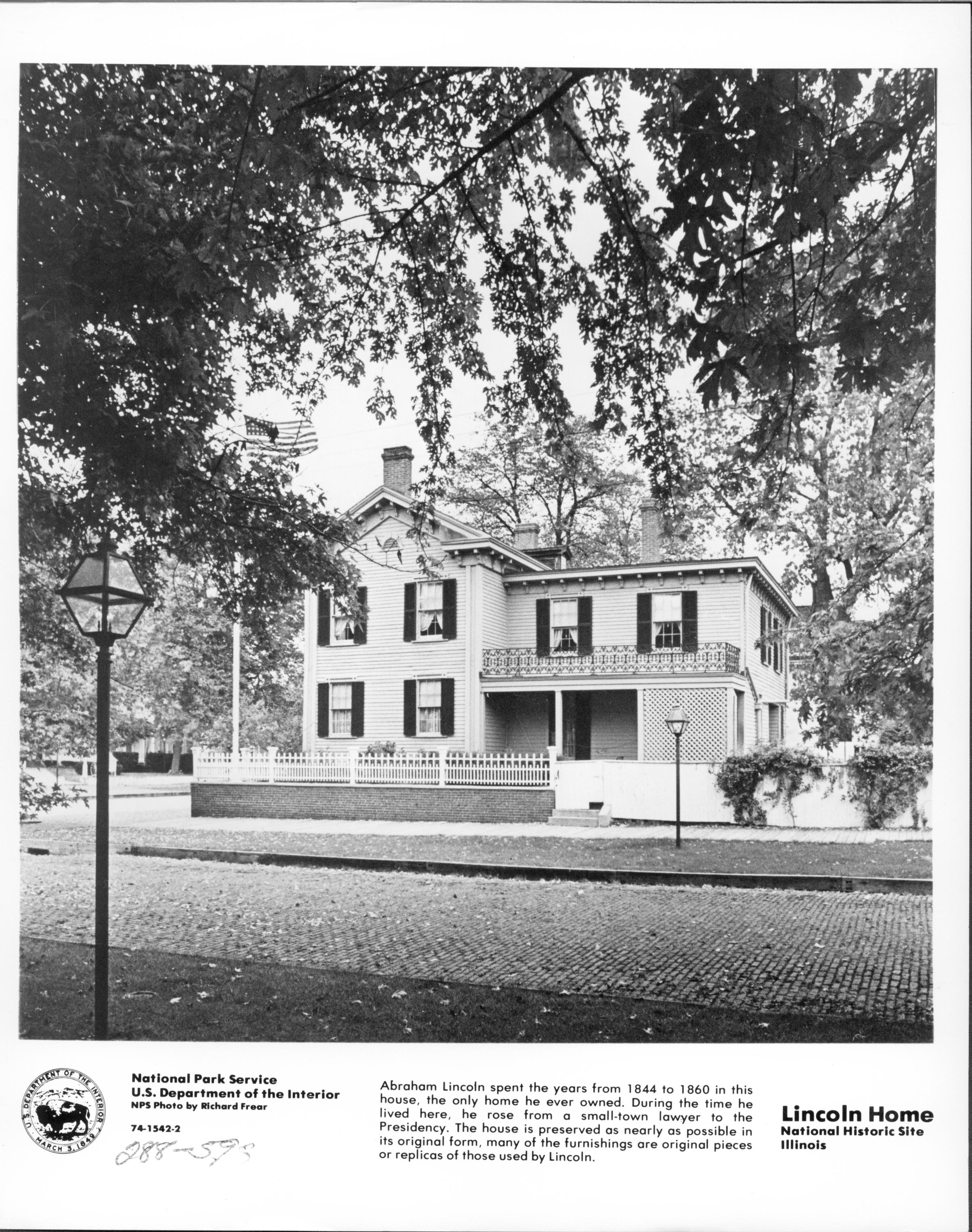Official Lincoln Home photo showing South elevation. Jackson Street in foreground bricked over. Dean House in far background left. Flagpole flying US flag in corner behind fence. Information about site and logo for Dept. of Interior on information bar at bottom. Looking Northwest from south of Jackson Street Lincoln Home, Jackson, flagpole, Dean