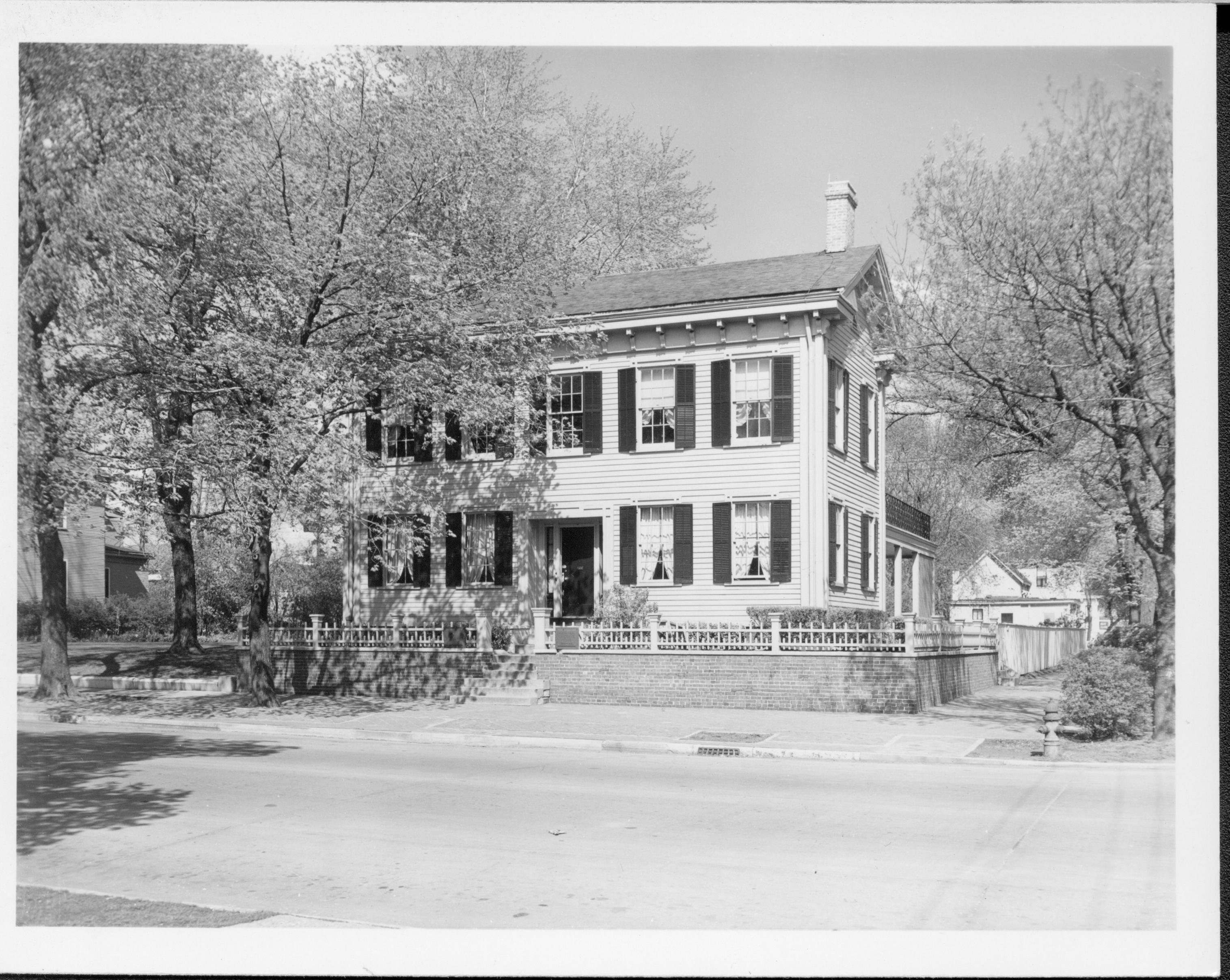 Lincoln Home west (front) elevation in summer, with several trees around it.  Fire hydrant on corner.  Two story houses on far left in Bugg lot (Block 10, lot 5) and Kercheval lot (Block 10, lot 9). Paved street. House appears to be painted white. Looking Northeast from 8th and Jackson Street intersection Lincoln Home, Bugg, Kercheval, paved street, fire hydrant, painted white