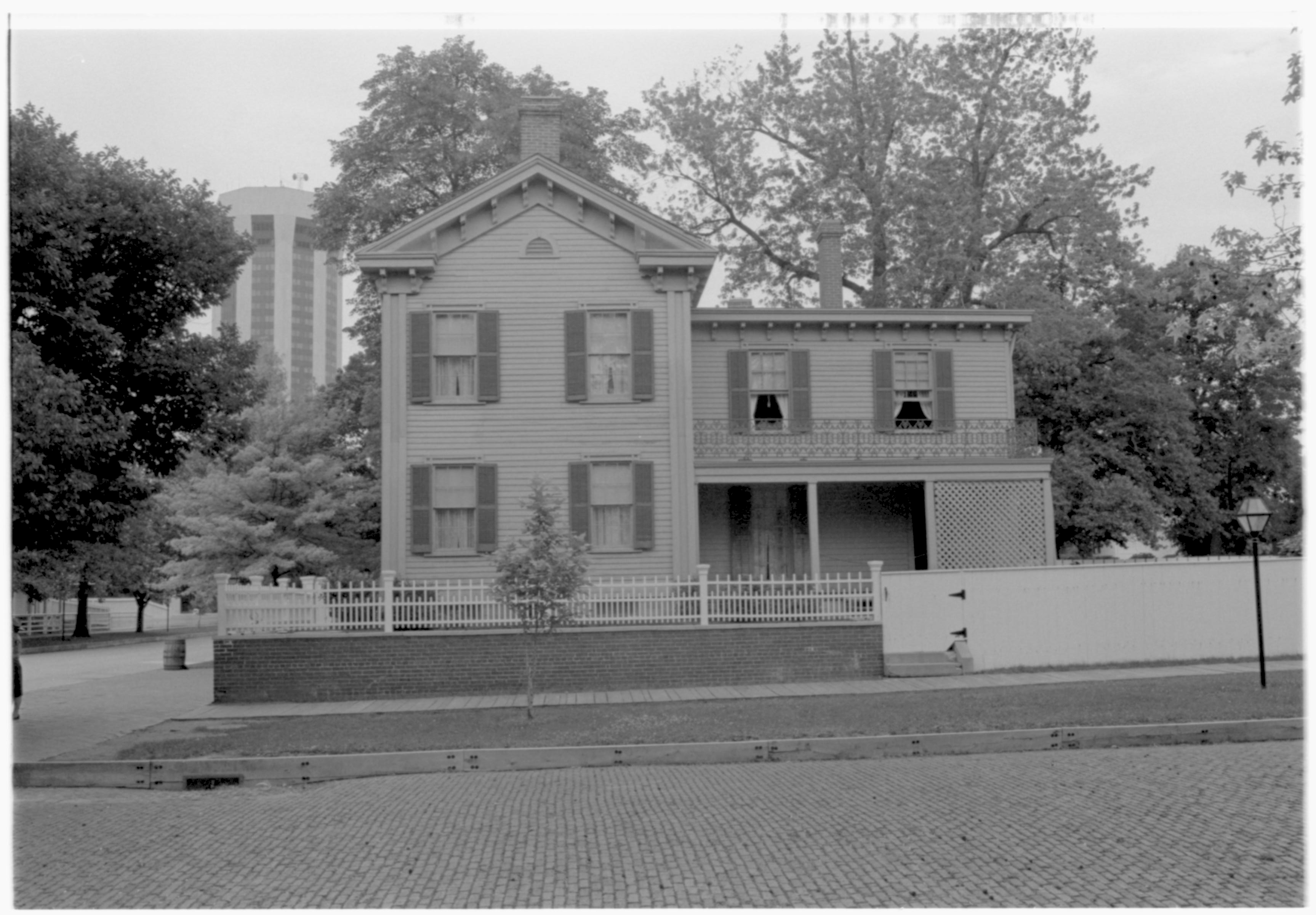 Lincoln Home South elevation. Jackson Street in foreground is bricked over. Several large trees surround the Home. Hilton Hotel Tower visible in far background left. Ranger Ruth Ketchum (?) barely visible on far left. Looking North from South of Jackson Street Lincoln Home, Jackson, staff, Hilton Hotel