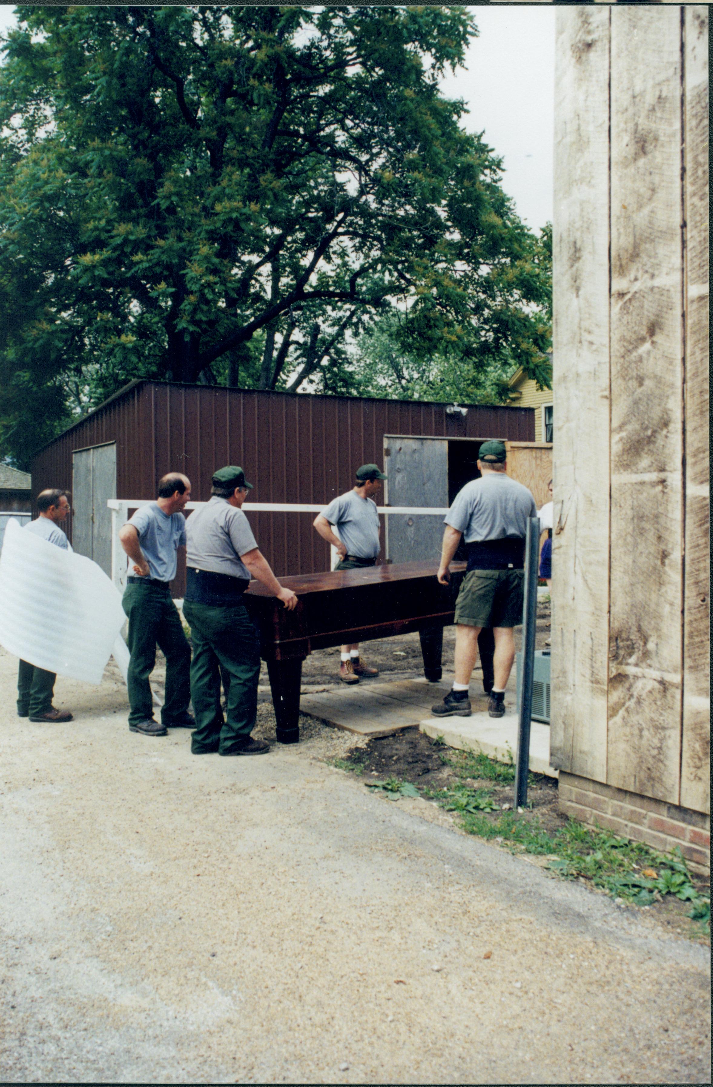 Members of maintenance moving piano from East alley onto the Arnold Lot in preparation to move into barn storage space. Boardwalk and building entrance are on South side of the barn Lincoln Home NHS, 1998 CRS Collection Move, East end of lot, Roll N7, exp 11 sheet 4 of 9 Carriage House, storage room