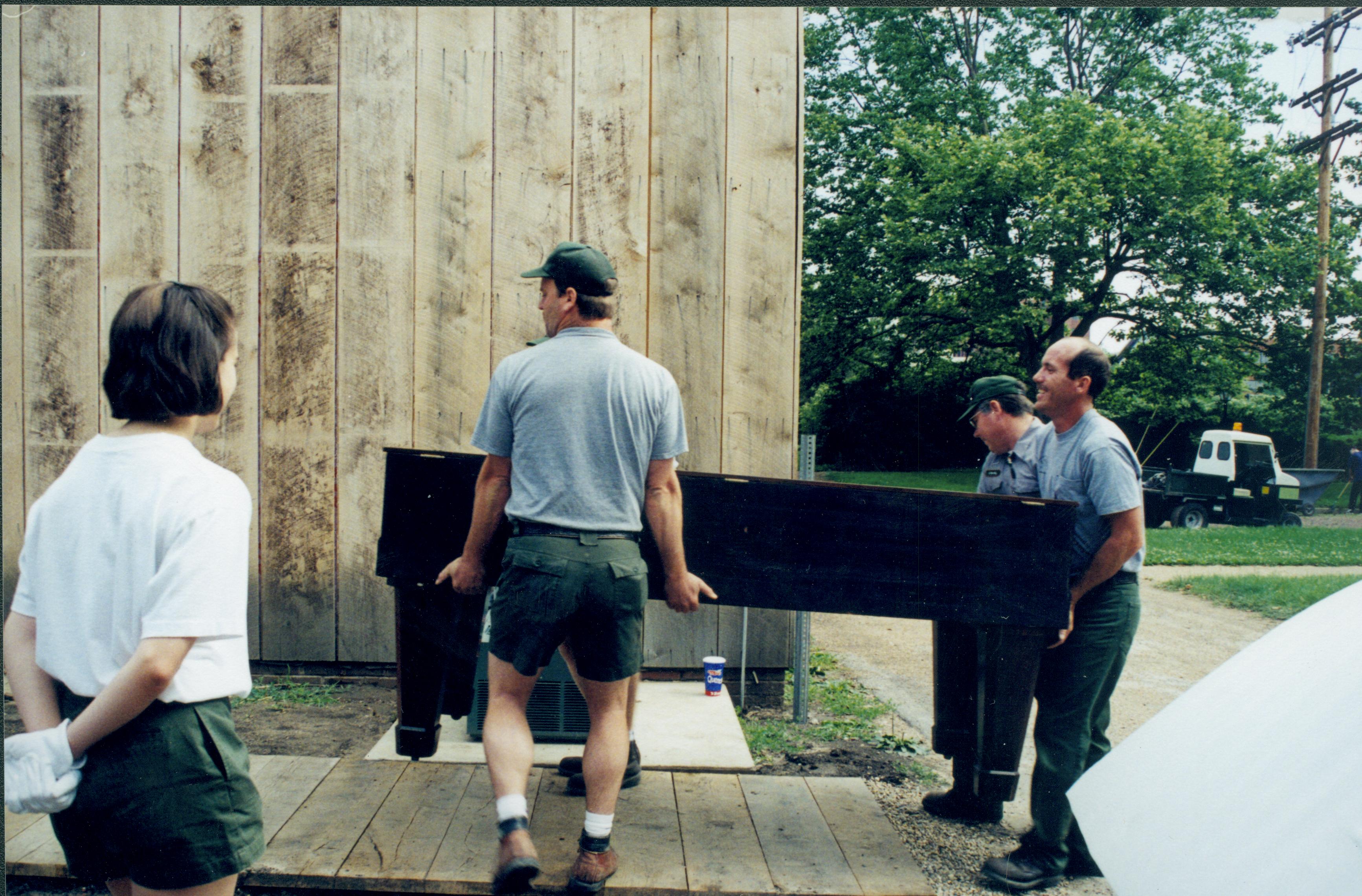 Members of maintenance moving piano from East alley onto the Arnold Lot in preparation to move into barn storage space. Boardwalk and building entrance are on South side of the barn Lincoln Home NHS, 1998 CRS Collection Move, East end of lot, Roll N7, exp 12 sheet 4 of 9 Carriage House, storage room