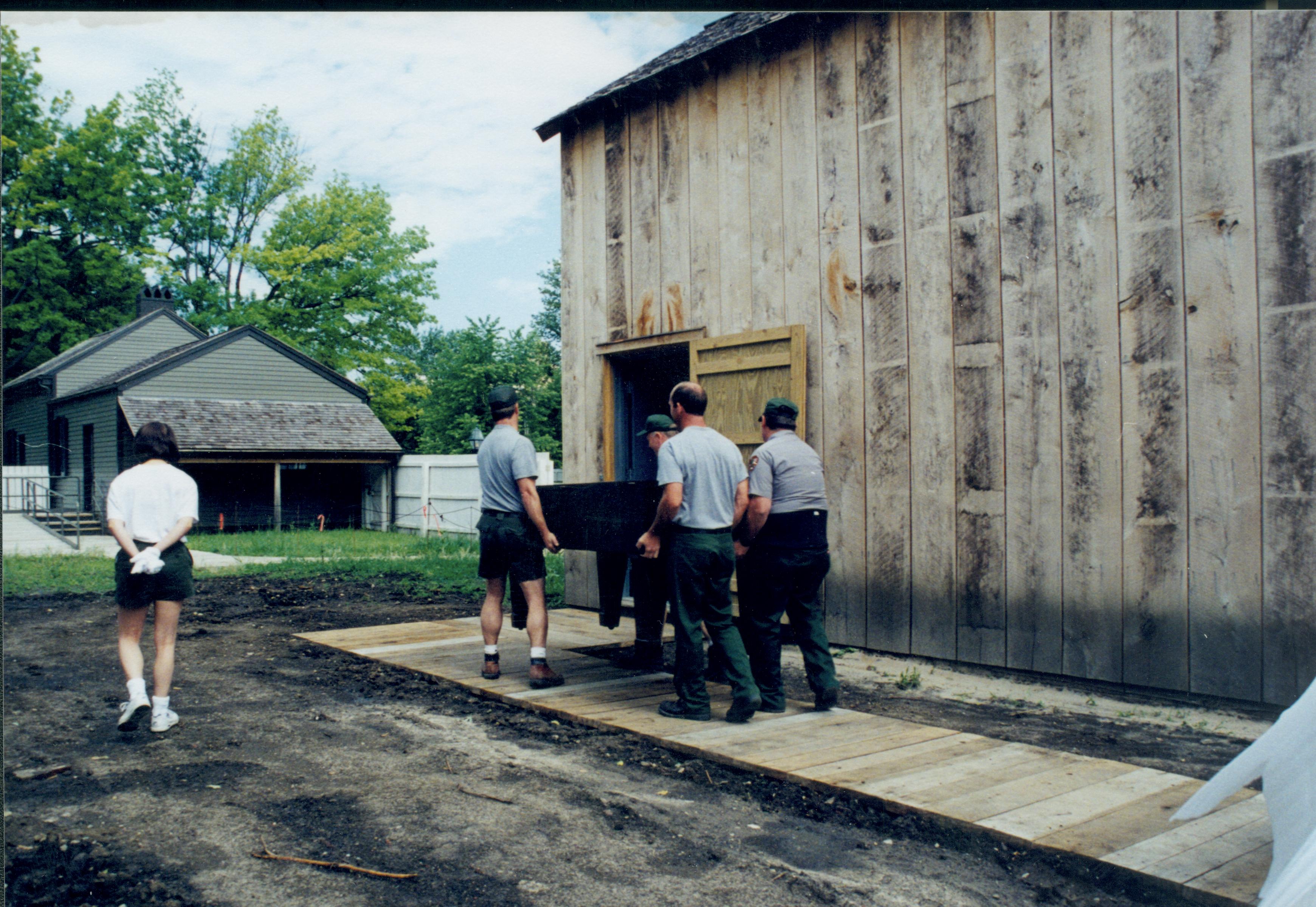 Members of maintenance moving piano from East alley onto the Arnold Lot in preparation to move into barn storage space. Boardwalk and building entrance are on South side of the barn Lincoln Home NHS, 1998 CRS Collection Move, East end of lot, Roll N7, exp 13 sheet 5 of 9 Carriage House, storage room