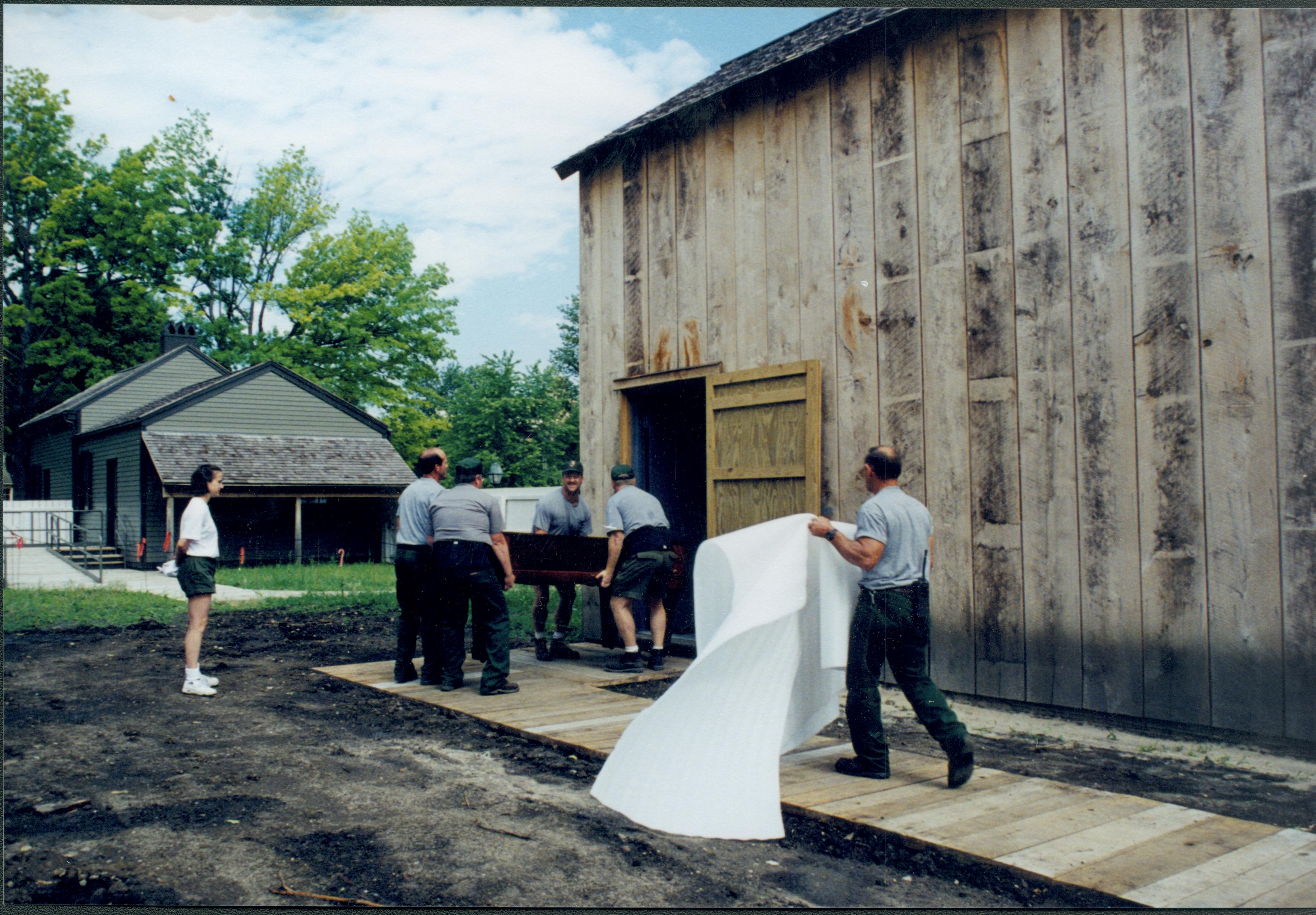 Members of maintenance moving piano from East alley onto the Arnold Lot in preparation to move into barn storage space. Boardwalk and building entrance are on South side of the barn Lincoln Home NHS, 1998 CRS Collection Move, East end of lot, Roll N7, exp 14 sheet 5 of 9 Carriage House, storage room