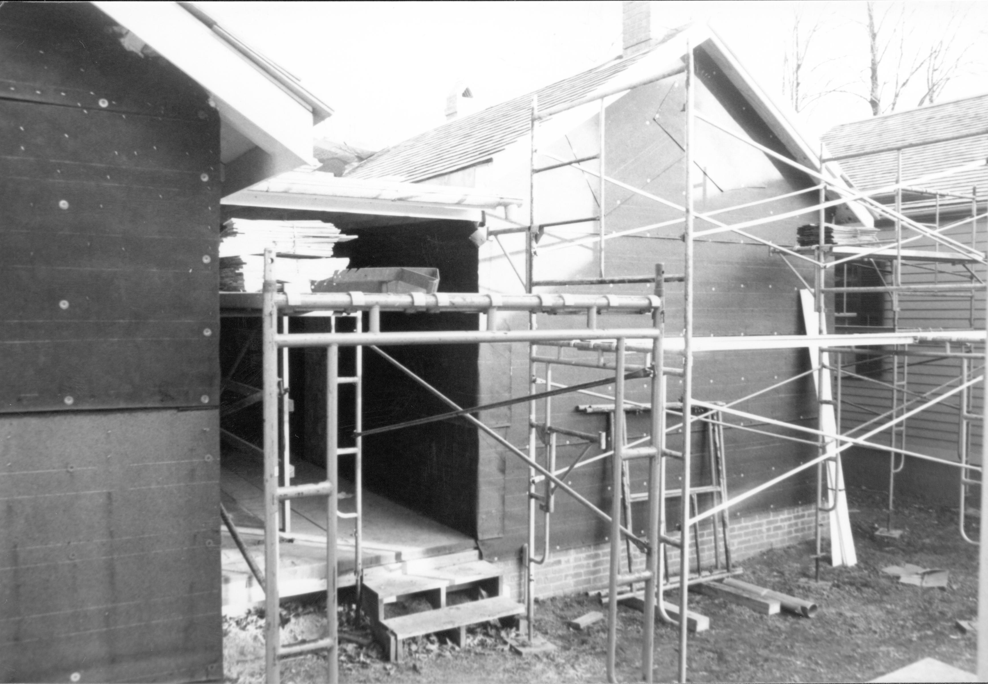 Corneau - restoration, close-up of scaffolding on West elevation. Steps lead to open, covered back porch. Sprigg House in background right. Temporary Restroom in foreground on far right. Looking Southeast on ladder in Corneau Lot (Block 6, Lot 16) Corneau, restoration, scaffolding, temporary, restroom, Sprigg