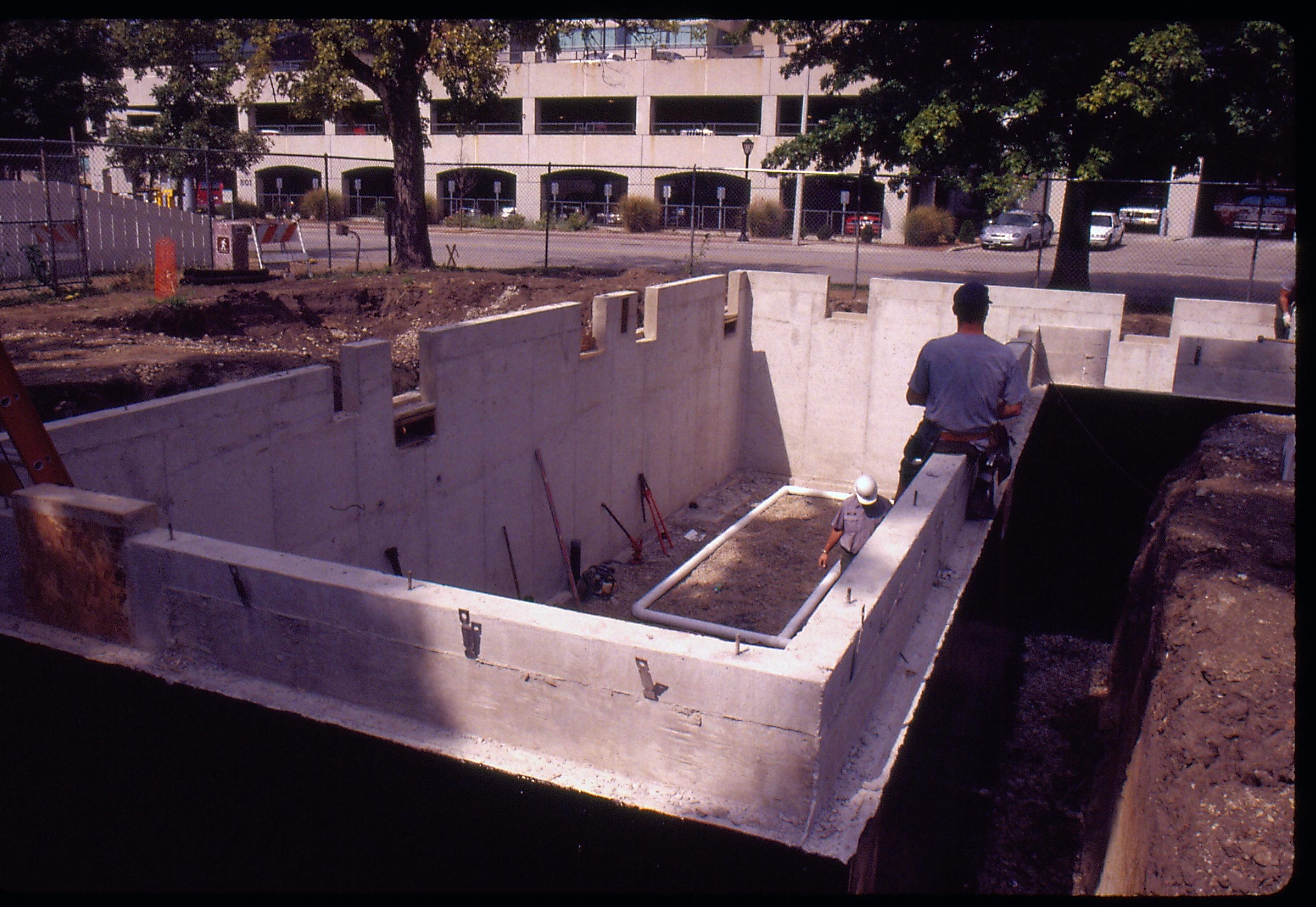 Morse - basement excavation, Walls poured. Maintenance workers ? and Sam Blasingame break out forms. Maintenance Work Leader Vee Pollack? checks pipe on floor. City parking garage in background  Looking North/Northwest from Morse Lot (Block 10, Lots 15-16) Morse, foundation, walls, staff, parking garage, pipes