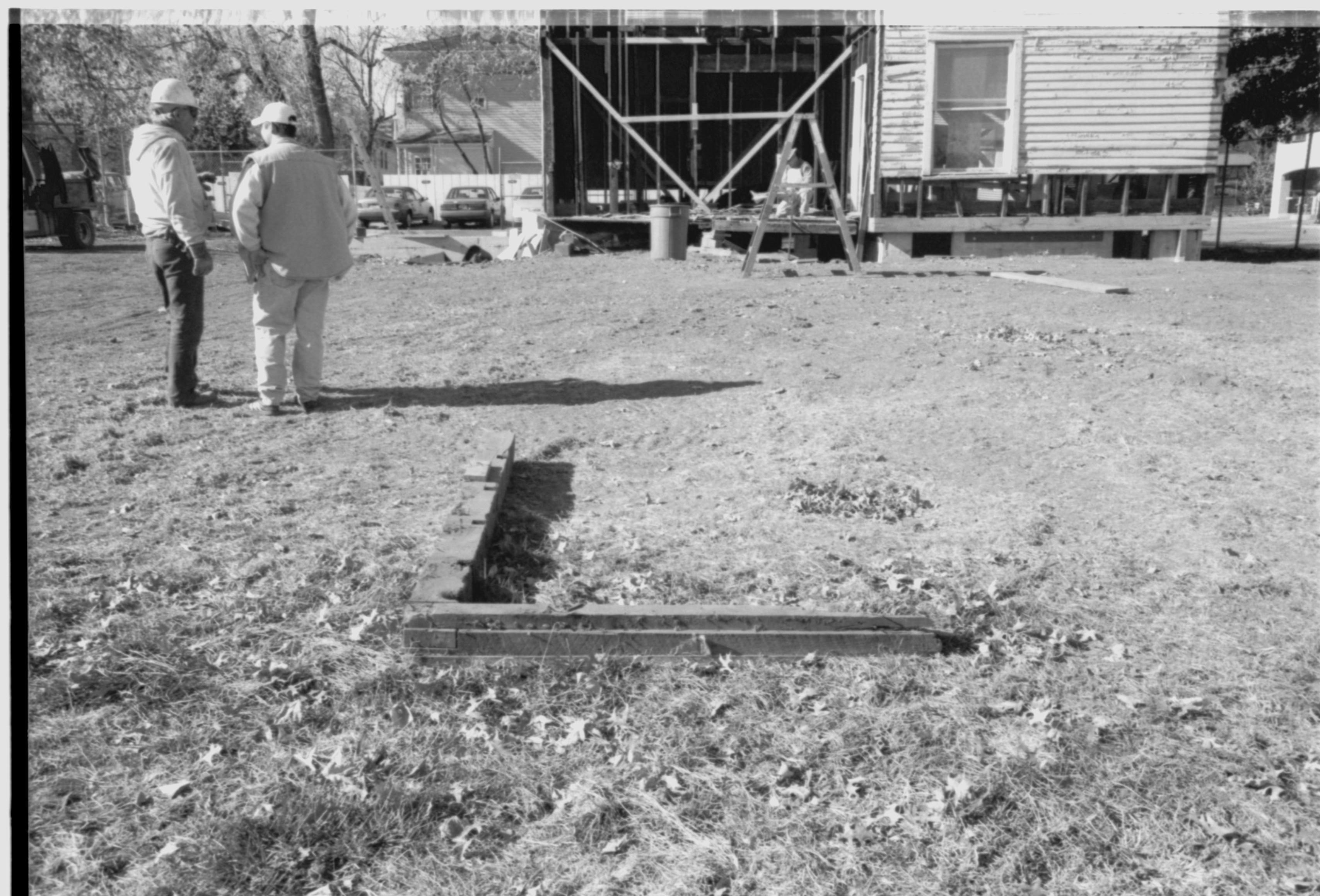 Morse - restoration, modern sill beam removed. Originally located in Southeast corner of house affiliated with an enclosed porch. Came off corner seen directly behind sill-black construction paper and V-shaped cross beams is back wall of open porch. Maintenance worker Eric Turner? visible on remains of modern porch.  Contractors chat on left. Conference Center visible behind Morse house in background center left. Looking West from Morse lot (Block 10, Lots 15-16)  Morse, restoration, sill, porch, contractors, staff, Conference Center