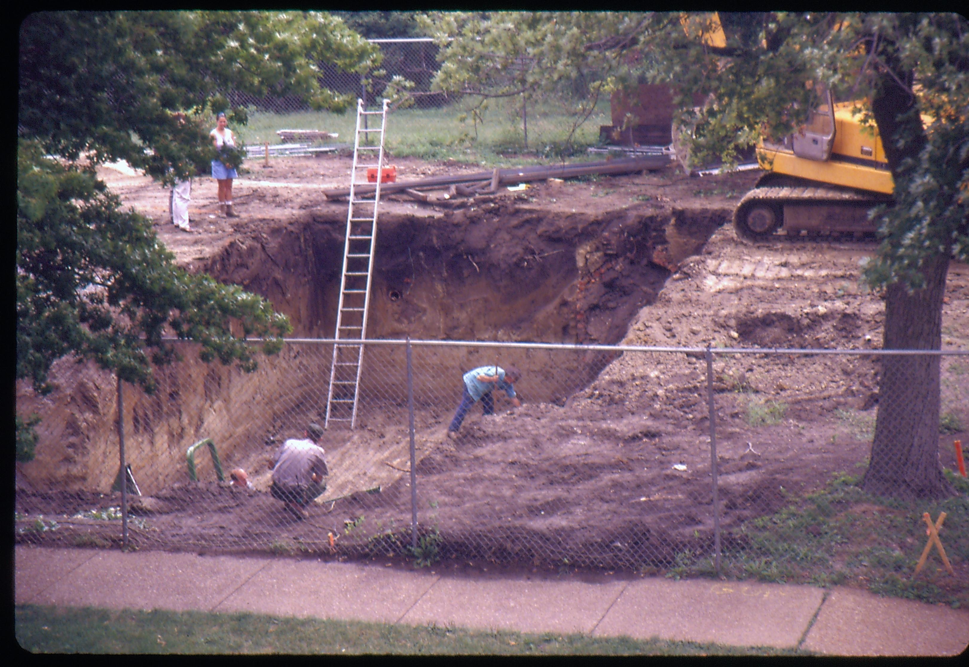 Morse - basement excavation. Fever River Archeologist Floyd Mansberger excavates top of the cistern (not visible) while Maintenance workers Al McHenry and Doug Sharp wait and Fever River staffer takes pictures while talking to Historian Tim Townsend and Curator Susan Haake in left background behind tree. Looking South from top of parking garage across Capitol Ave. Morse, foundation, archeology, staff, Fever River, parking garage, Capitol Ave.