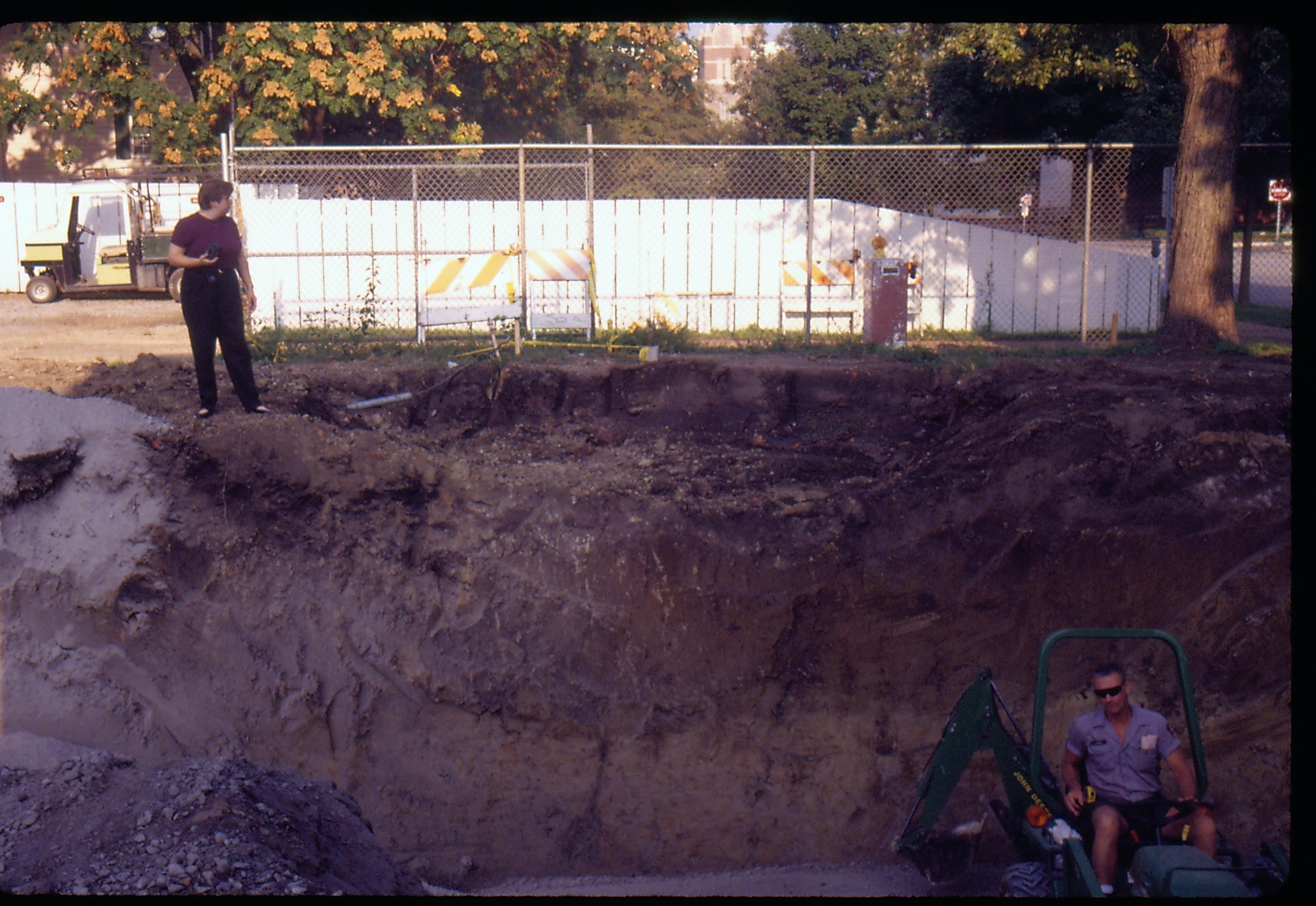 Morse - Basement elevation. Maintenance worker Ed Smith spreads gravel and sets wall footings in basement before the concrete pour.  Curator Susan Haake documents the project with photos while standing on edge. Conference Center in background. Looking West from Morse Lot (Block 10, Lots 15-16) Morse, basement, foundation, staff, Conference Center