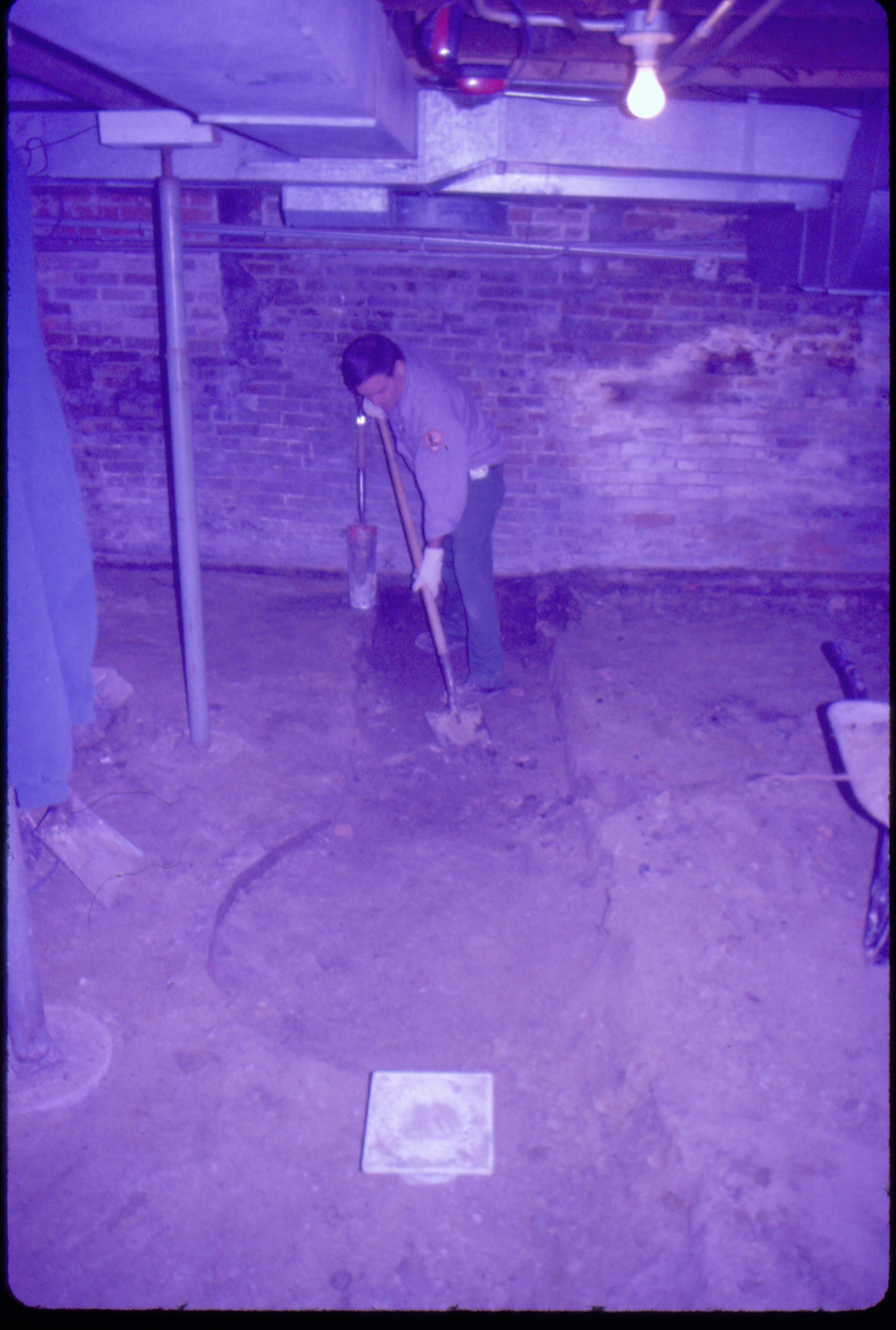 Lyon House - basement, Brick-lined cistern (or gravity furnace) remnants. Maintenance Worker Tom Pacha digs out part of basement floor to find full extent of brick-lined utilities. Metal supports on left, duct work overhead, square drain cover in foreground. Brick wall in background. Looking North in basement Lyon, Basement, cistern, brick wall, staff, duct work, utilities