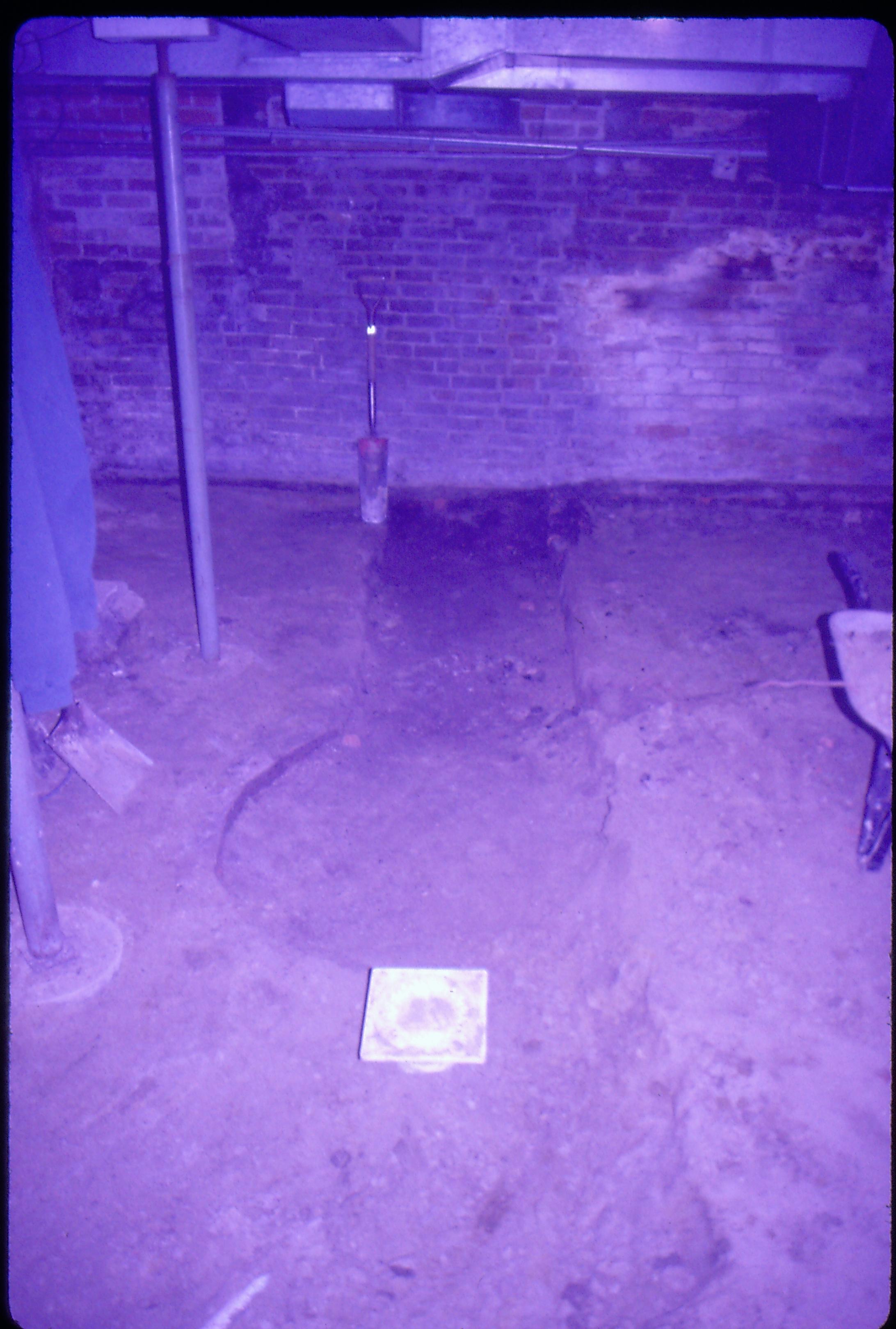 Lyon House - basement, brick cistern (or gravity furnace) remnants in floor. Metal supports on left--one has blue jacket hanging from it. Shovel in background leaning against brick wall, duct work on ceiling. Square plastic drain cover in foreground. Wheelbarrow on far right. Looking North in basement Lyon, Basement, brick wall, cistern, duct work, utilities