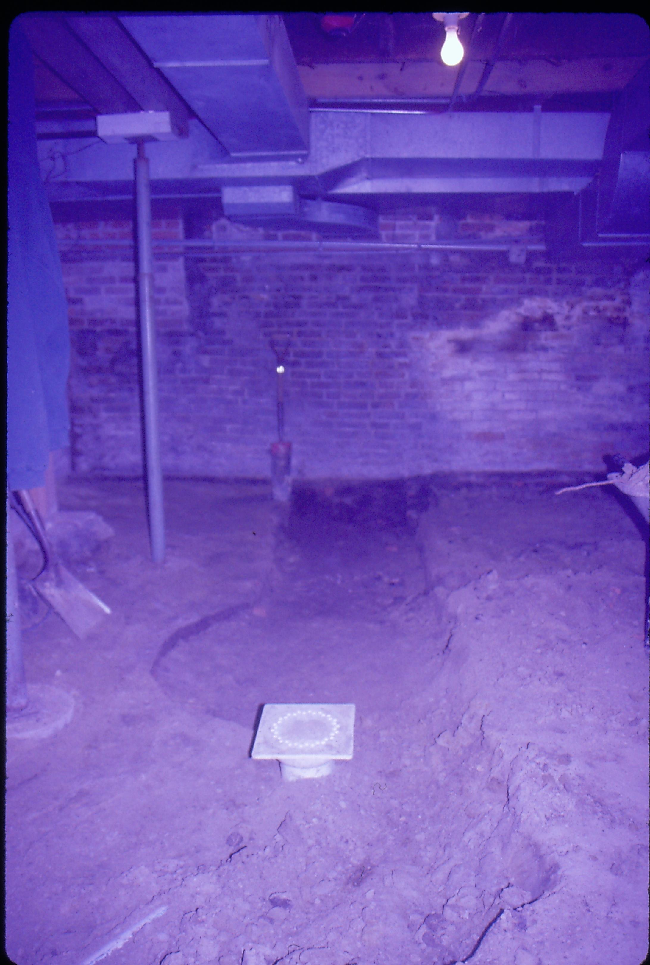 Lyon House - basement floor showing trench running throughout. Square plastic draing cover on edge of cistern/gravity furnace? remnant. Metal supports on left, duct work overhead. Shovels seen on left and leaning on brick wall in background Looking North in basement Lyon, Basement, trench, drain, duct work, cistern
