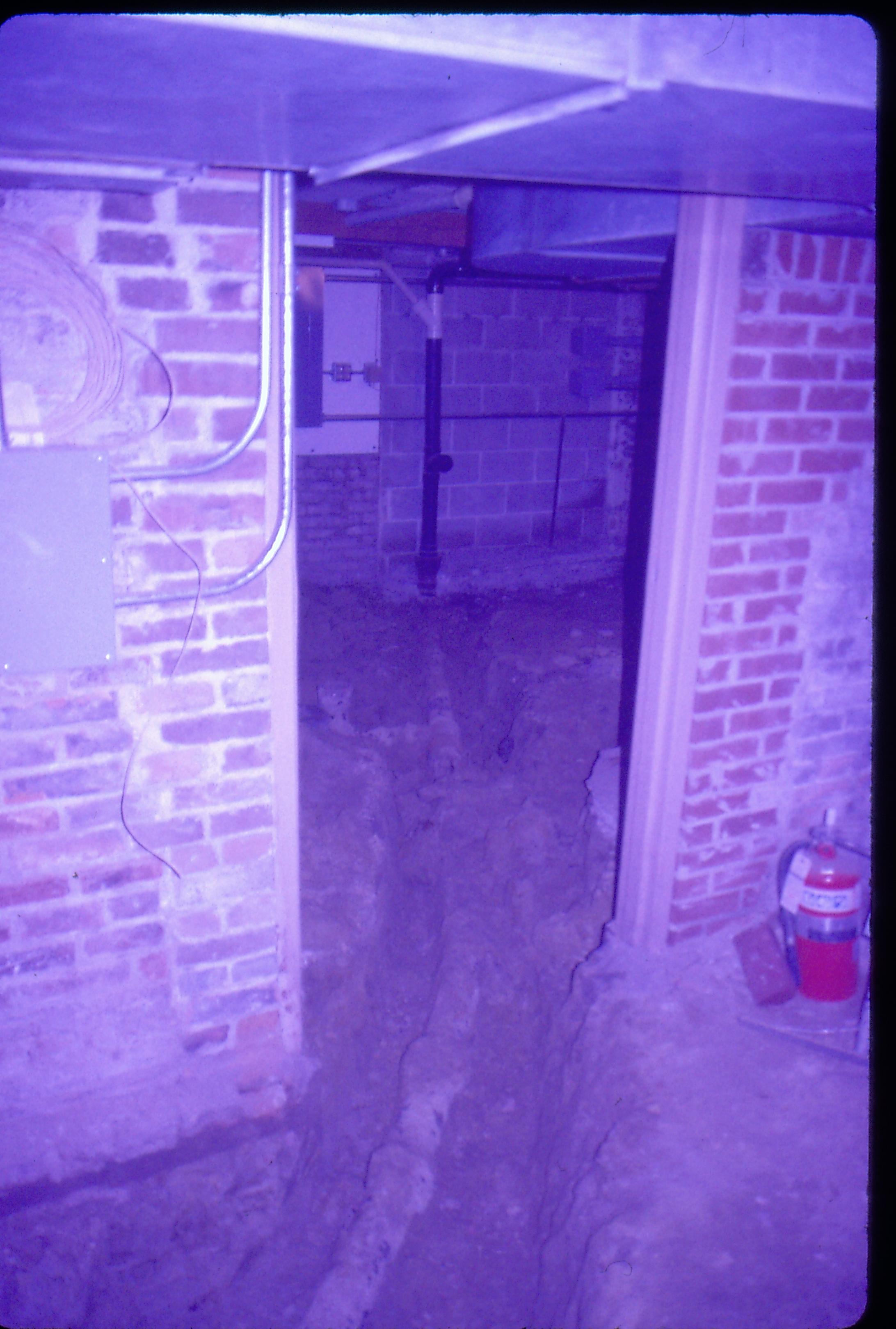 Lyon House - basement, trench dug to reveal old plumbing running under dirt floor in basement. Duct work on ceiling, conduit and pipes seen against walls in main area and furnace room. Fire extinguisher on far right. Looking Northwest into furnace room in basement Lyon, Basement, utilities, pipes, brick walls, cinder block, plumbing